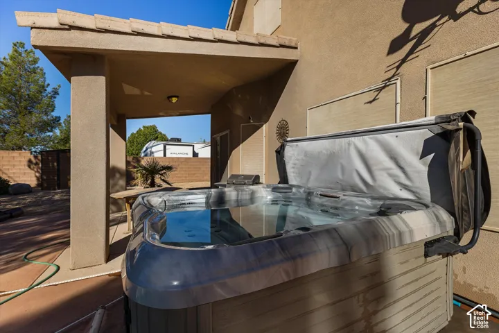 Covered patio with a built-in spa, textured stucco exterior, and a privacy block wall