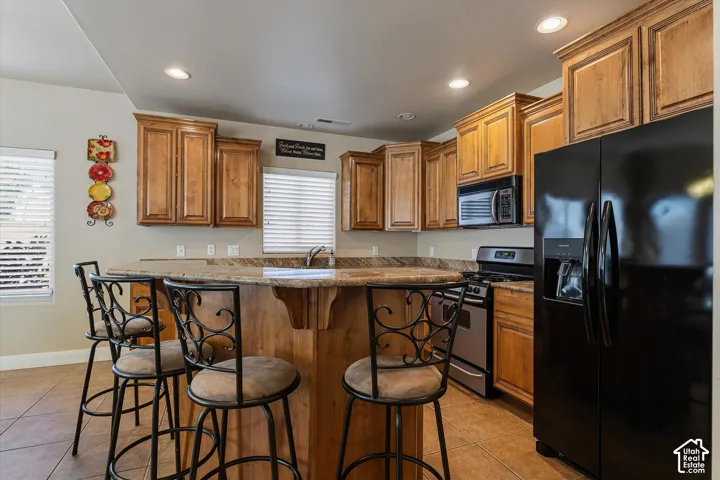 Kitchen featuring warm wood cabinetry, neutral countertops, a dedicated island, black appliances, and recessed lighting