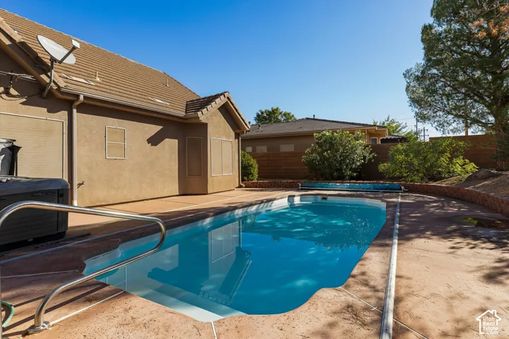 Concrete patio featuring an in-ground swimming pool with metal handrails