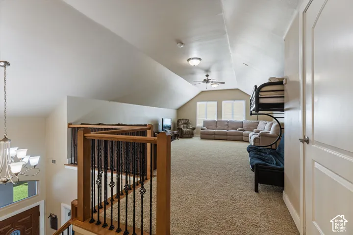 Spacious loft area with vaulted ceilings, neutral carpeting, and a ceiling fan