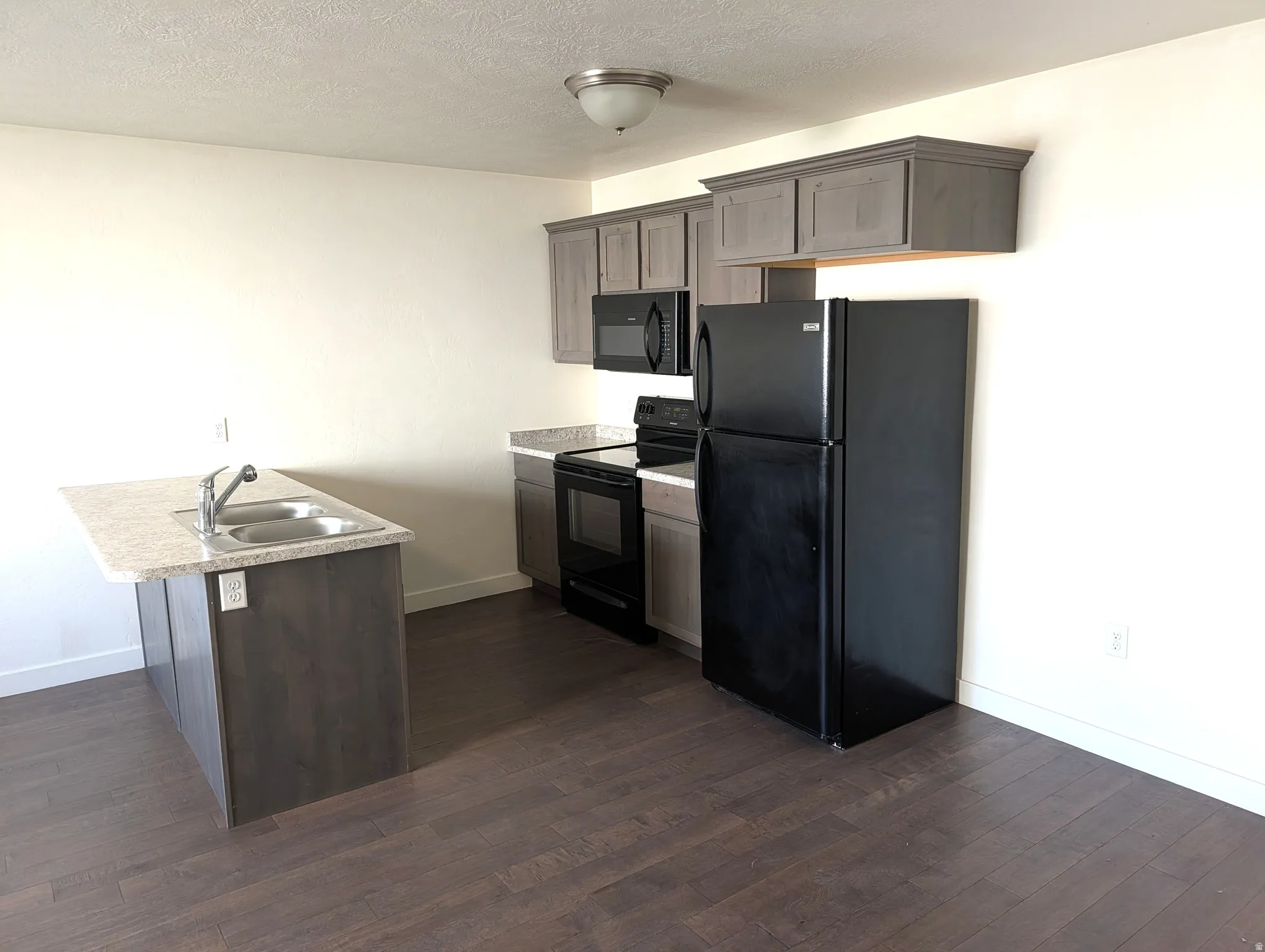 Kitchen featuring wood-finish flooring, gray cabinetry, a kitchen island with dual basin sink, and black appliances