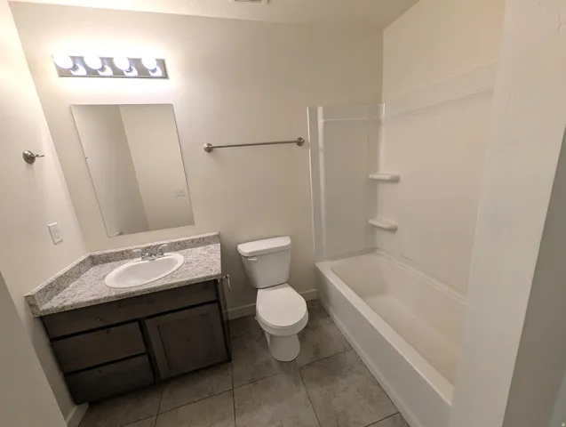 Bathroom featuring a vanity with an integrated sink, a full-width mirror, a toilet, and a bathtub with a shower surround