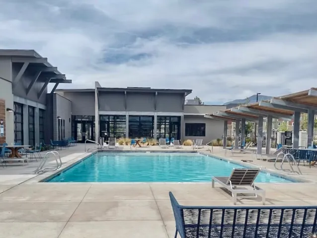 Outdoor swimming pool with concrete decking, a modern building with large glass panels, and covered outdoor seating areas