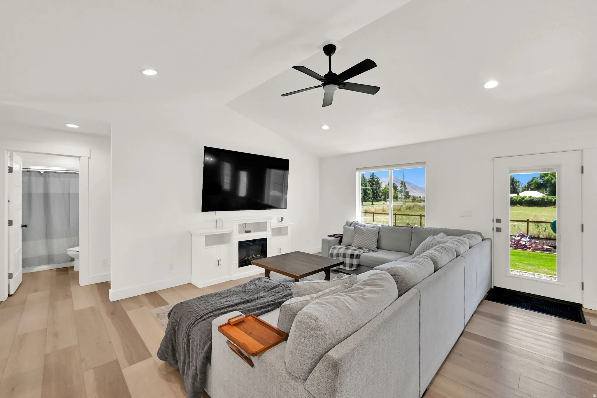 Vaulted ceiling with a ceiling fan, recessed lighting, wood-finish flooring, built-in entertainment center with a fireplace, and a glass-paned exterior door