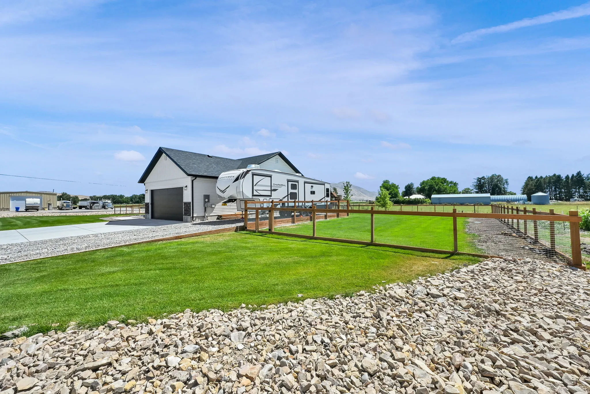 White exterior with dark trim, attached garage with dark door, paved driveway, and a fenced lawn area