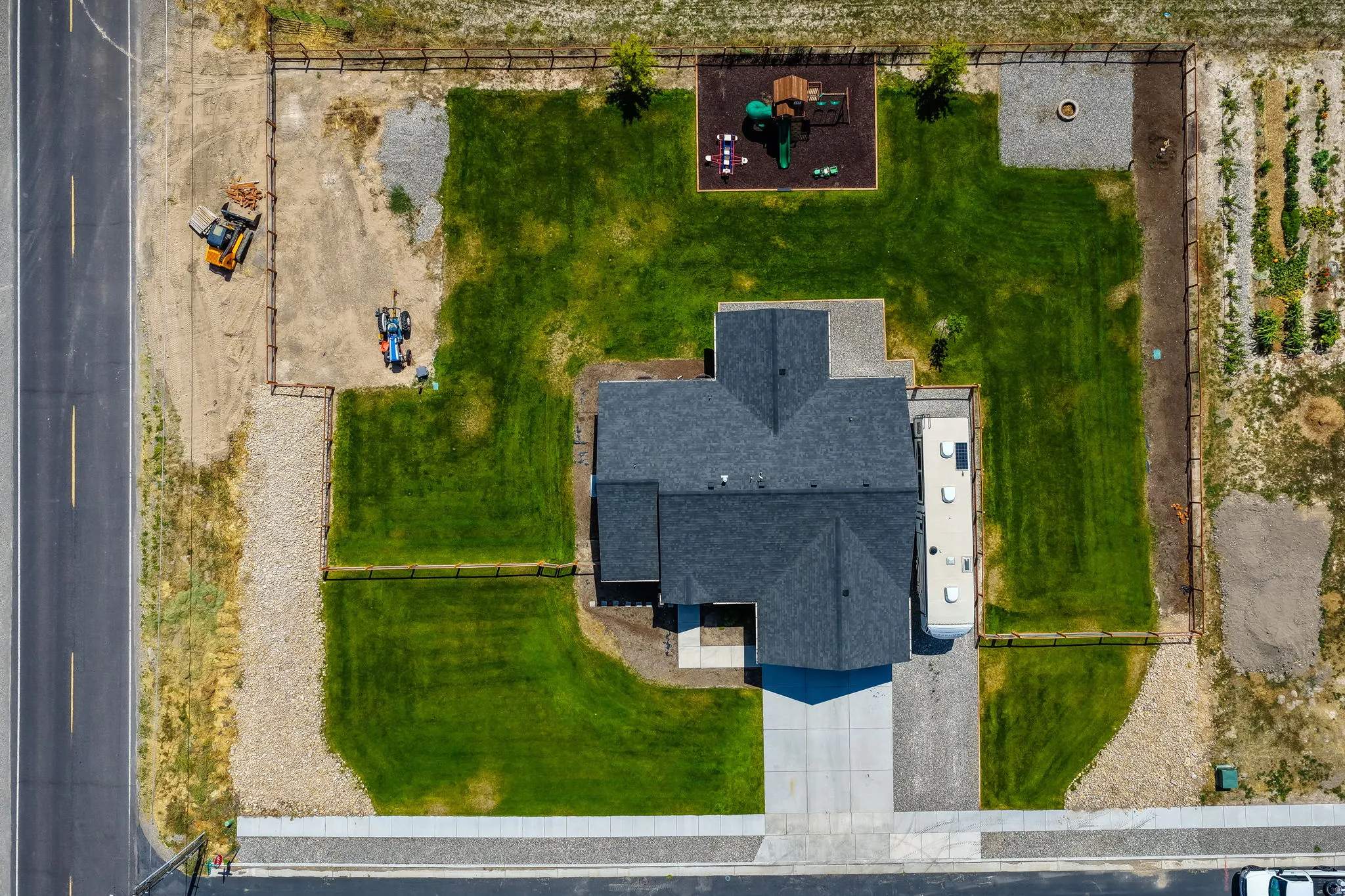 Expansive lawn space, concrete driveway, gravel landscaping, fire pit area, and a children's play structure