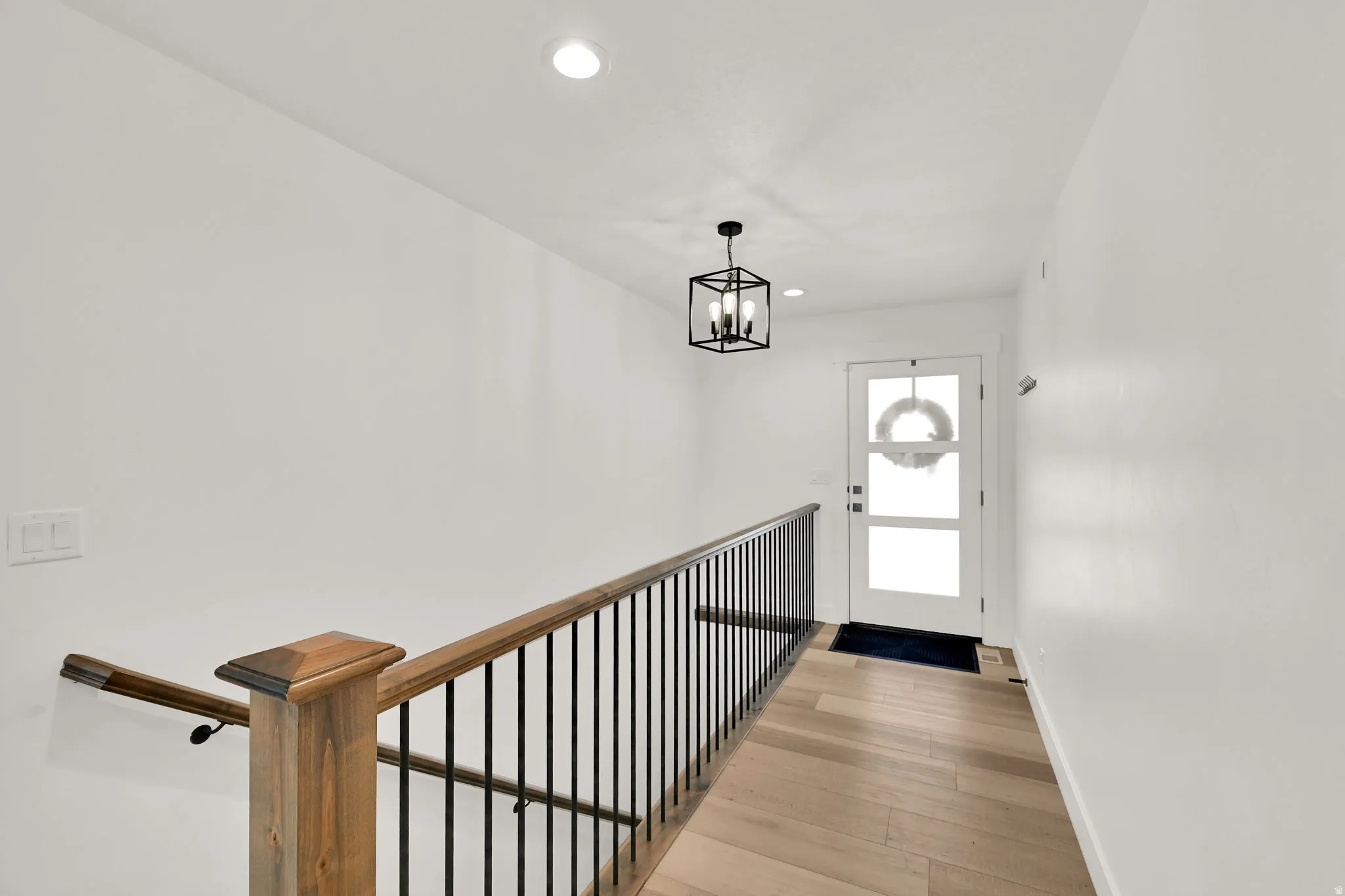 Entryway featuring wood-finish flooring, a contemporary black metal and wood staircase railing, a modern geometric pendant light, and a white paneled door with frosted glass inserts