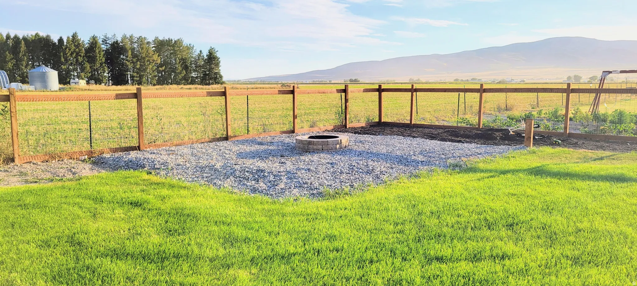 Expansive outdoor space featuring a wood-post fence, gravel patio area, and built-in fire pit