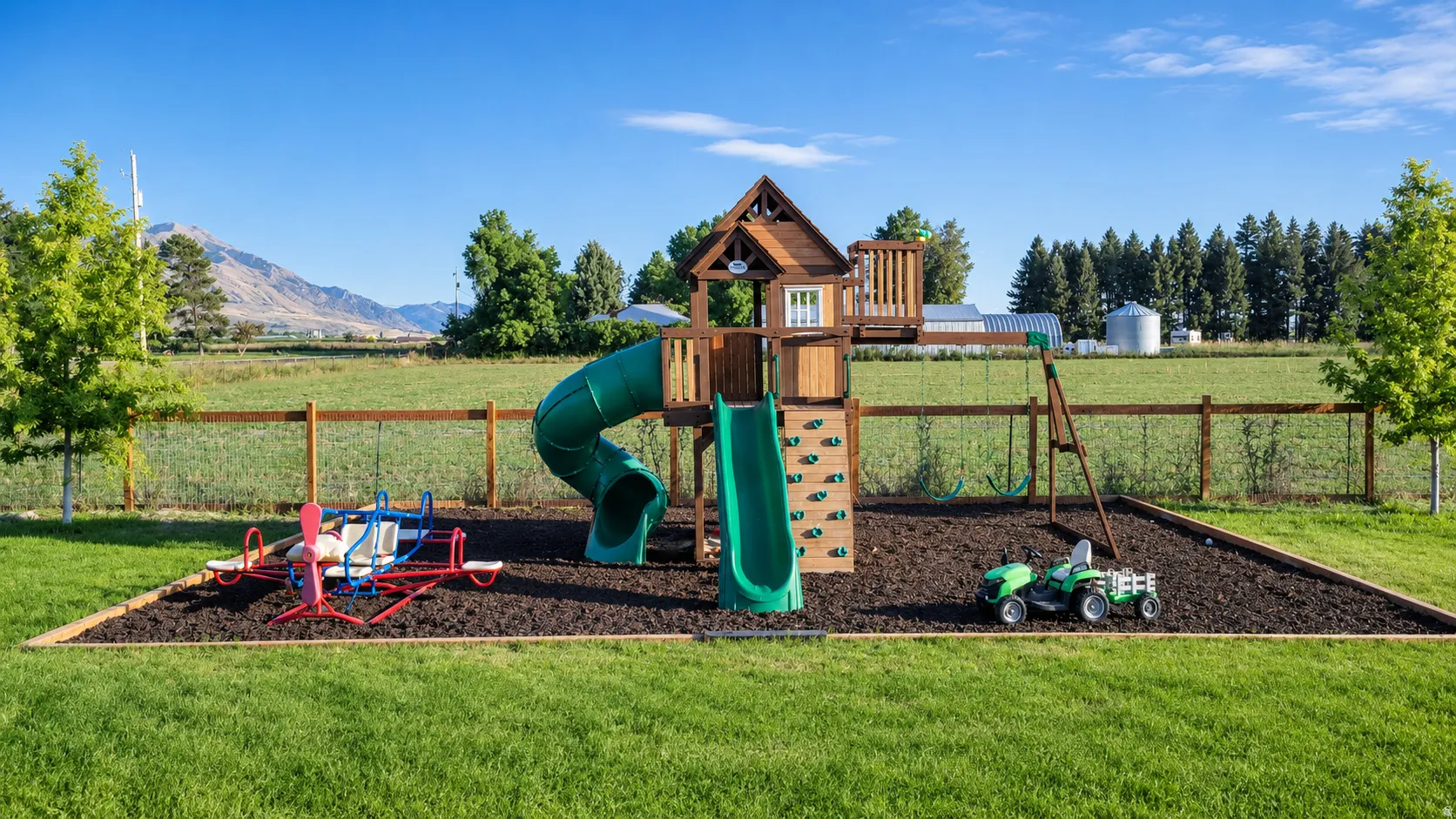 Expansive green lawn with a wooden playset featuring a slide and rock wall