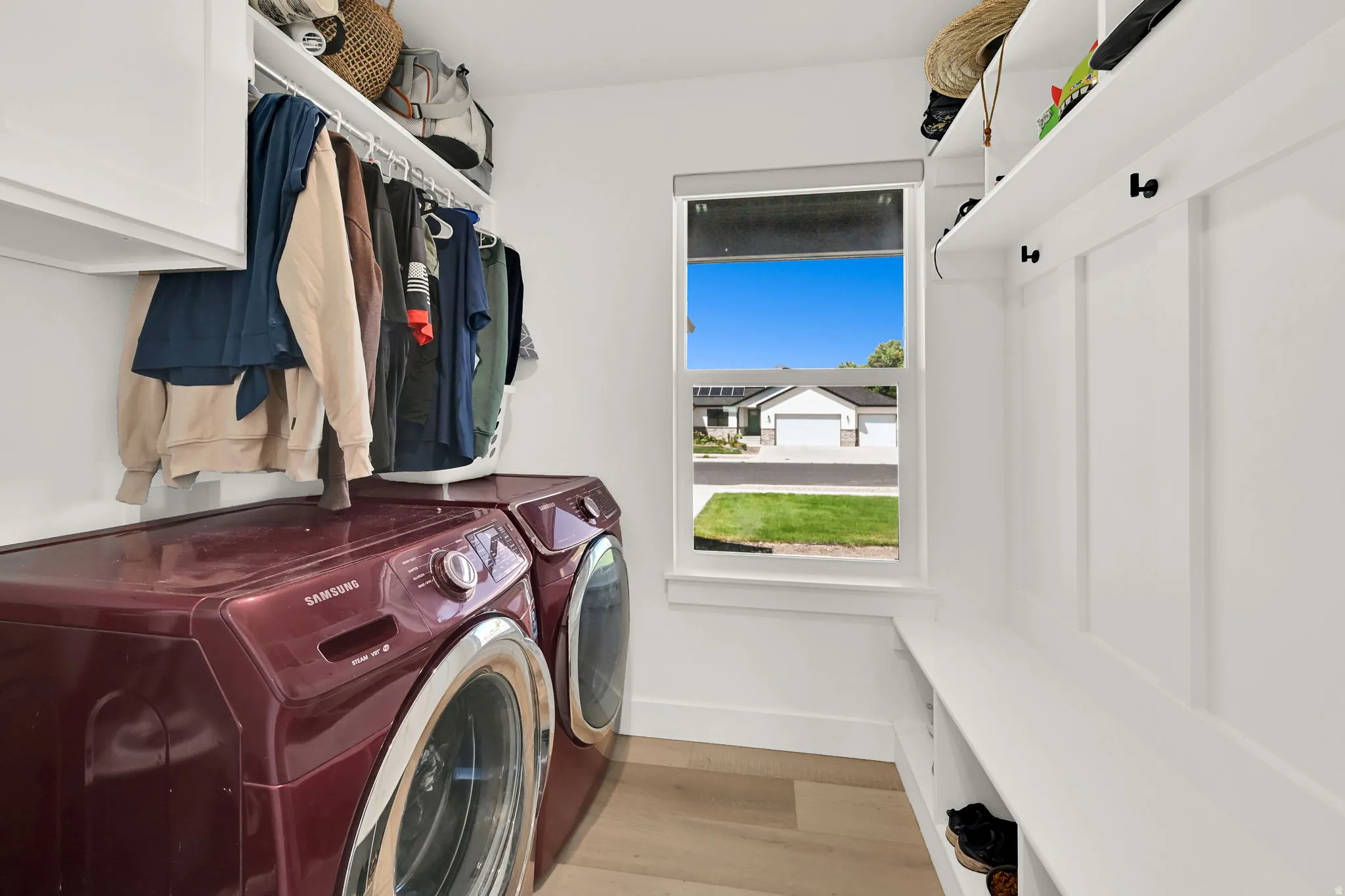 Dedicated laundry area featuring wood-finish flooring, built-in shelving, white cabinetry, and a window