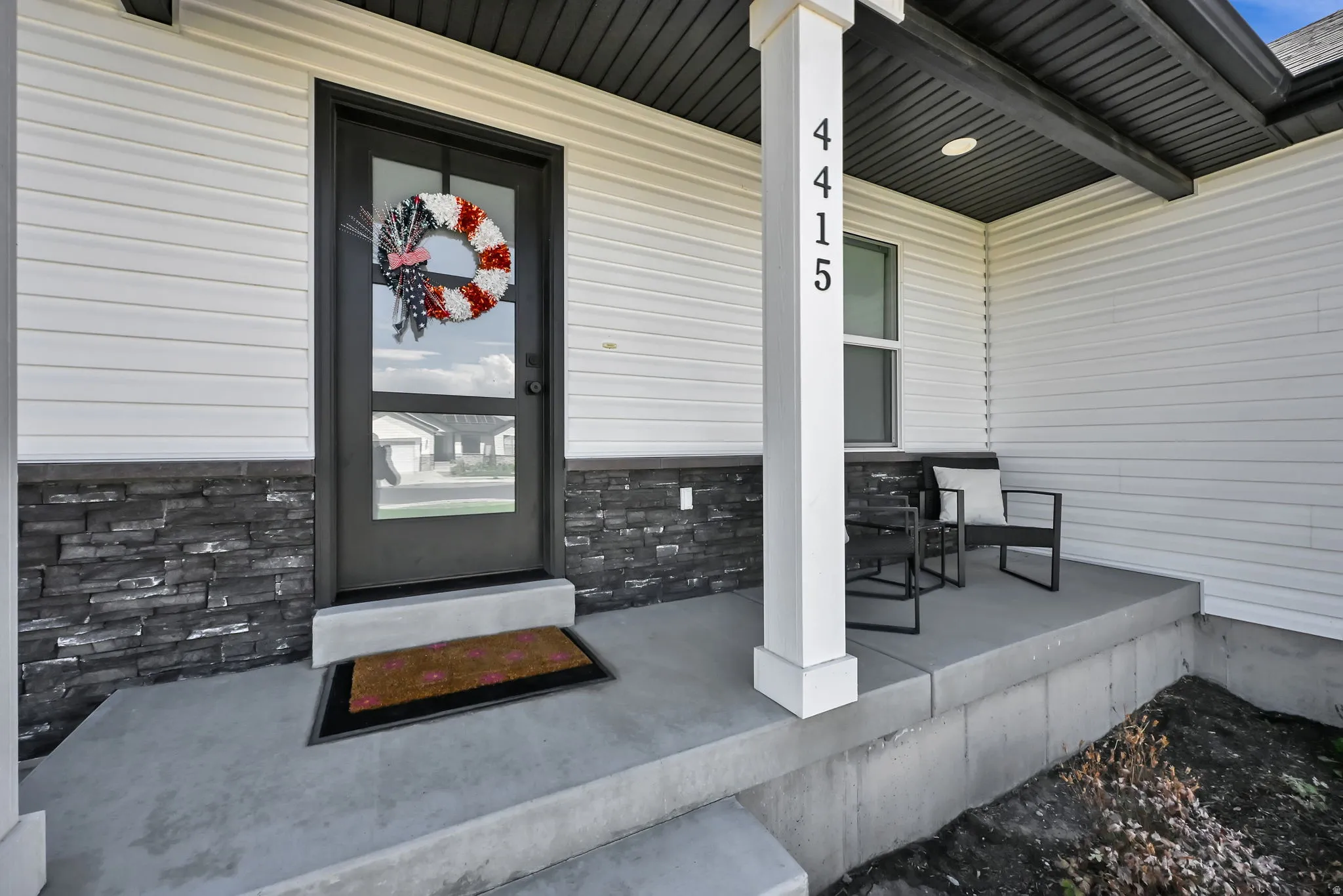 Front entry with white siding, dark stone veneer accents, and a dark-framed glass paneled door