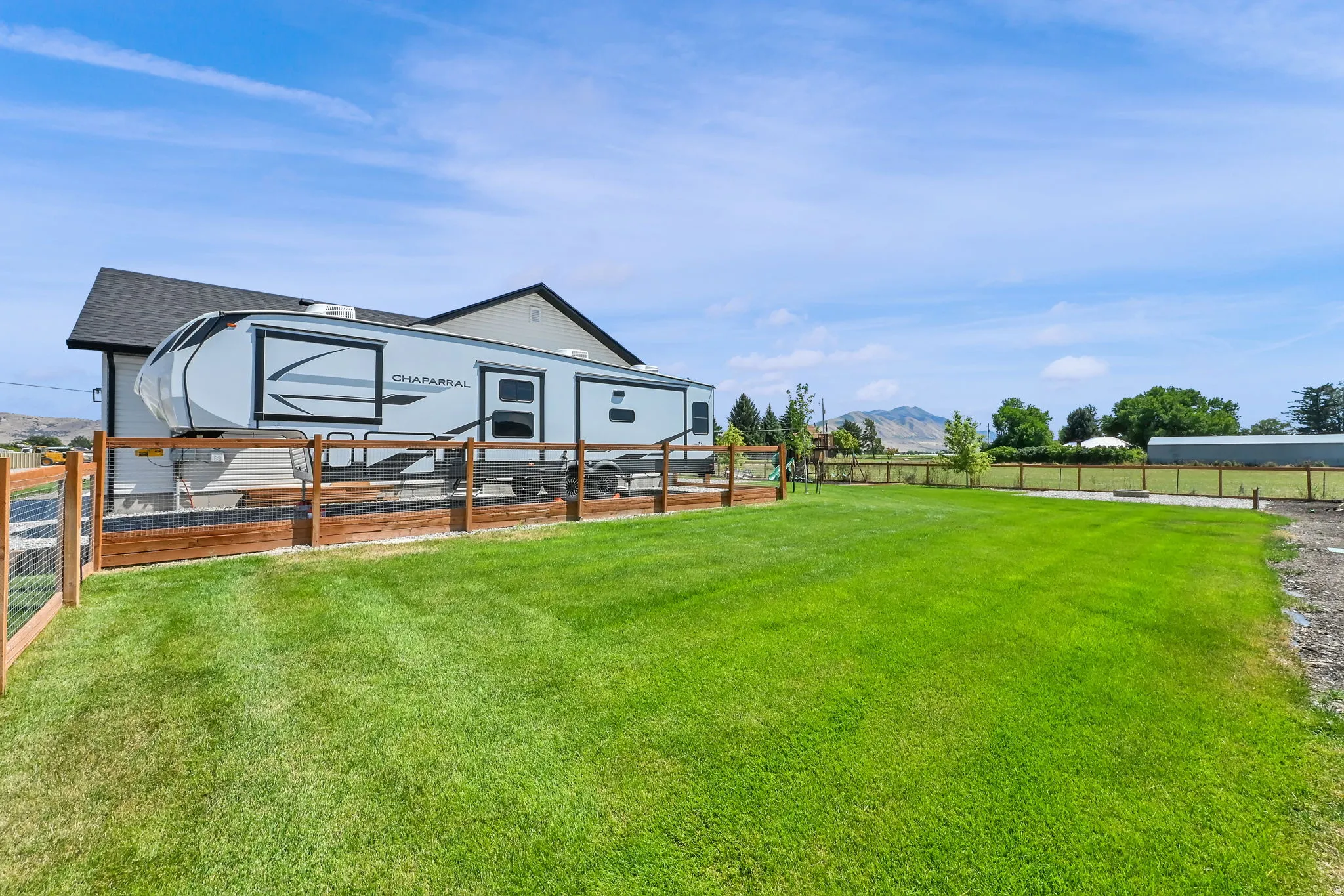 Expansive green lawn, wood fence with wire mesh, gravel area, and a backdrop of distant hills