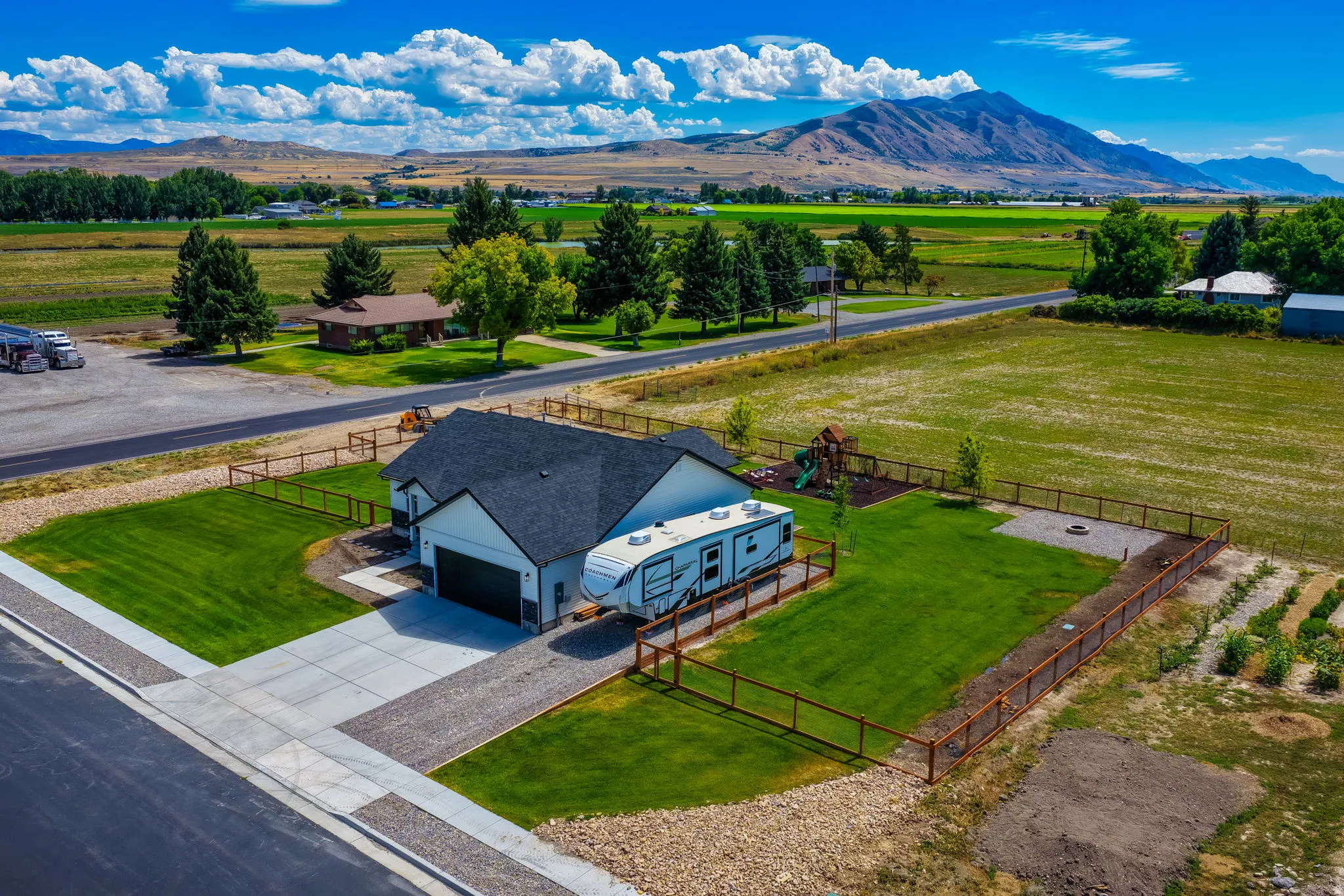 Expansive lawn, attached garage, concrete driveway, wood fencing, and mountain backdrop