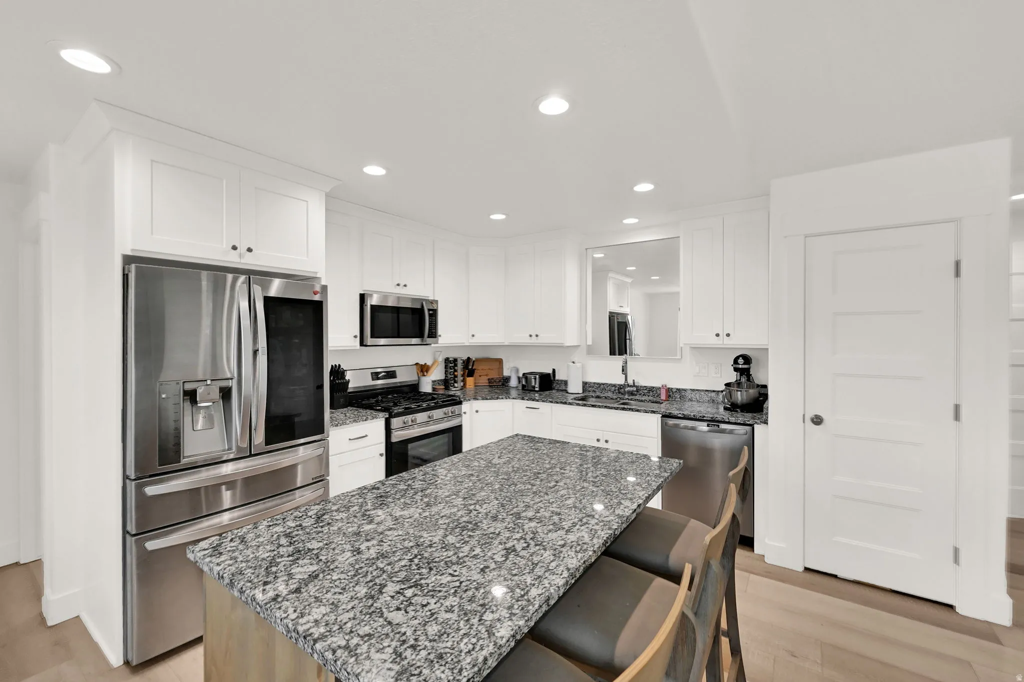 Kitchen featuring white shaker cabinetry, stainless steel appliances, recessed lighting, wood-finish flooring, and a large island with a stone countertop