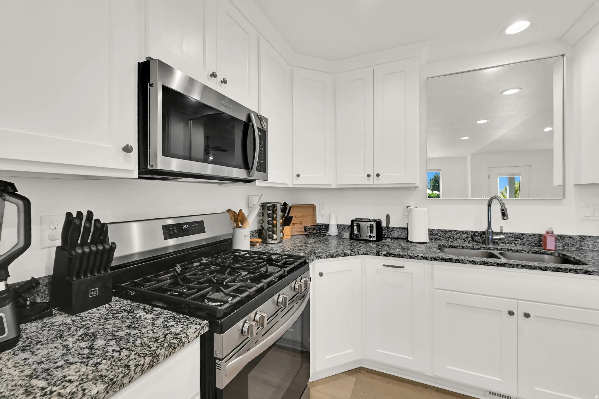 White shaker cabinetry, stainless steel appliances, dark speckled countertops, undermount double-basin sink, and a chrome gooseneck faucet