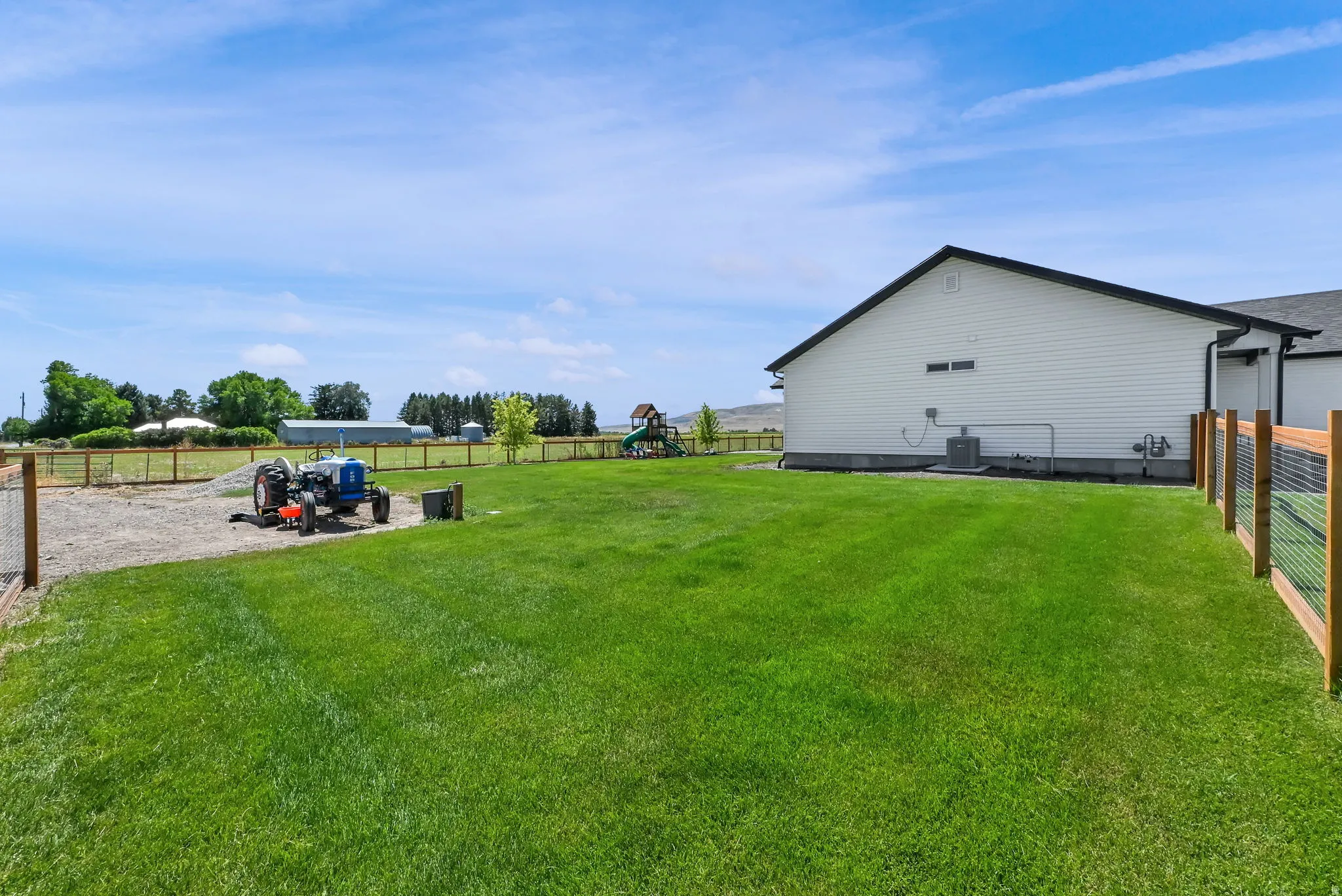 Expansive lawn area with a wood and wire fence, bordered by a gravel section