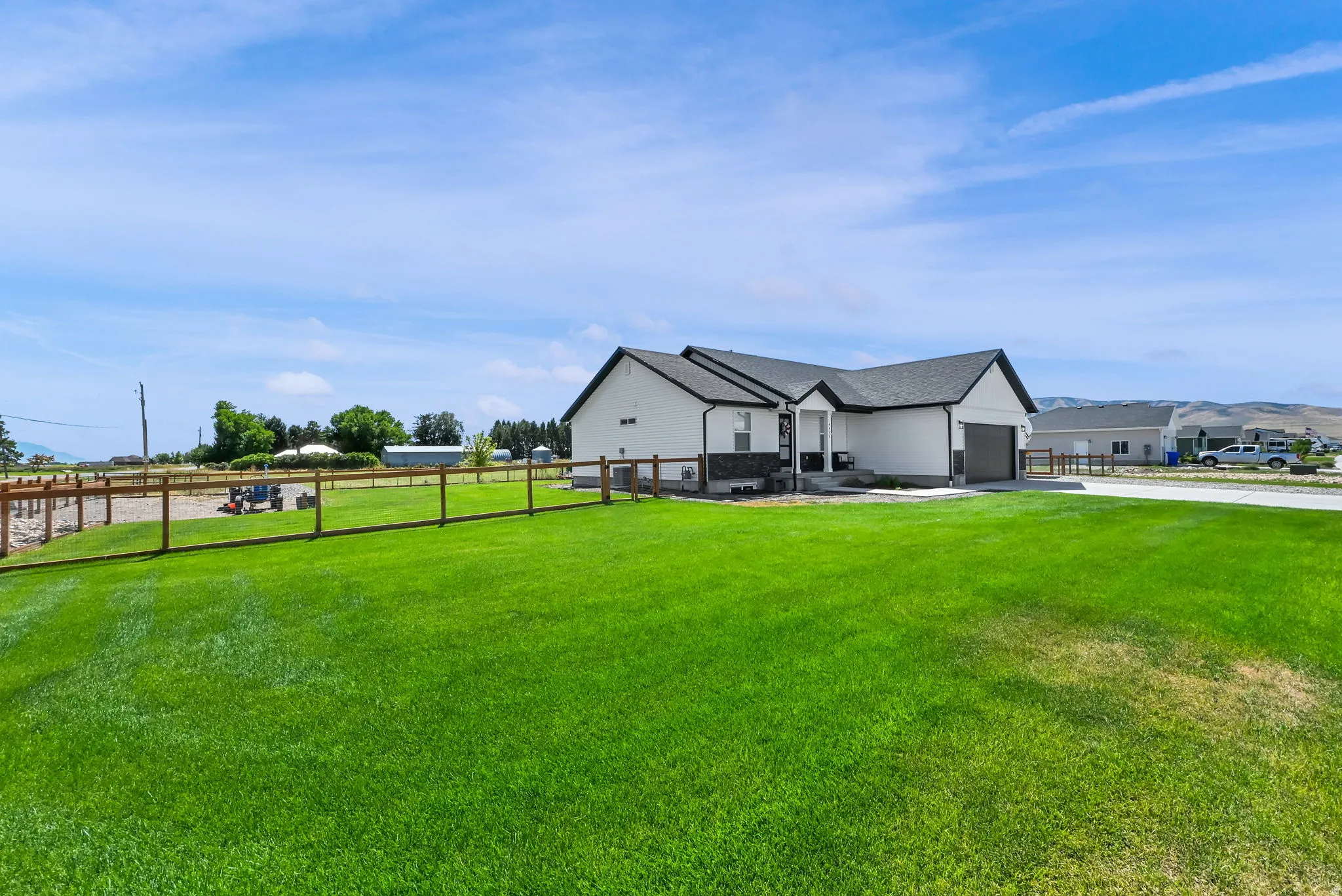 Expansive grassy lawn with a wood-post fence, contemporary single-story residence, and an attached two-car garage