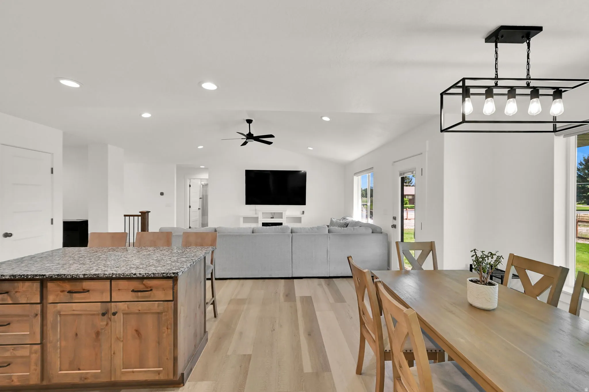 Open-concept living space featuring wood-finish flooring, recessed lighting, a ceiling fan, and a kitchen island with stone countertop and wood cabinetry