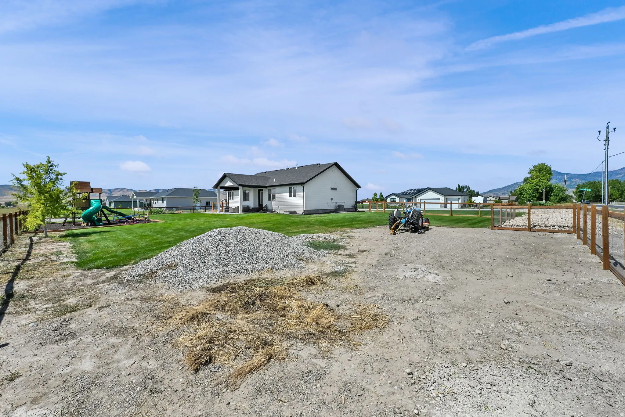 Expansive outdoor area featuring a wood fence, a large pile of gravel, and a level ground surface