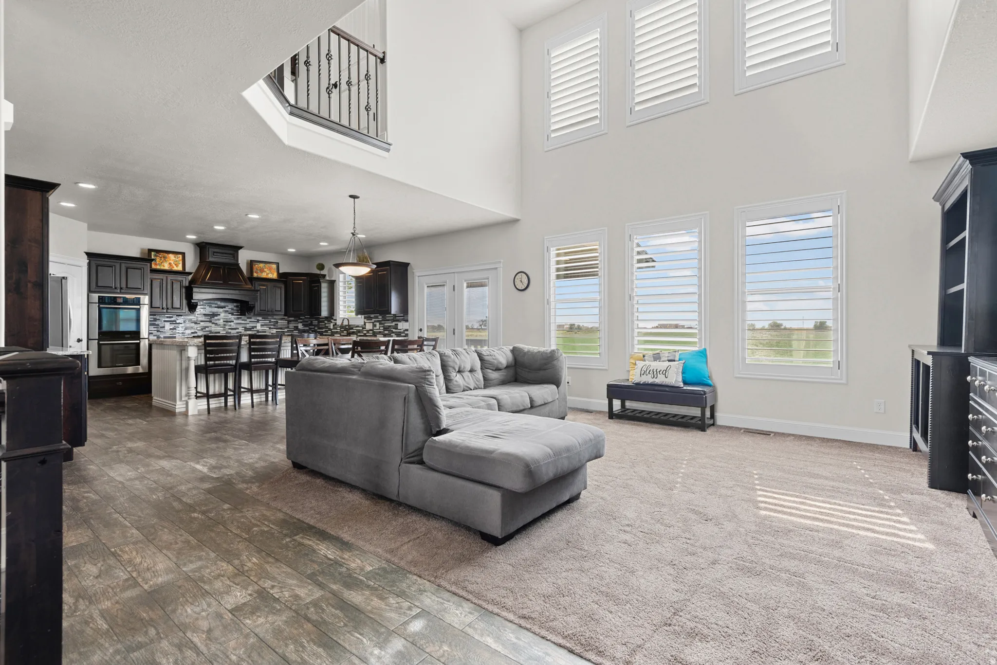 Open-concept living space featuring soaring ceilings with skylights, abundant natural light from multiple large windows, wood-finish flooring, a modern kitchen with dark cabinetry and stainless steel appliances, and a spacious great room with a fireplace