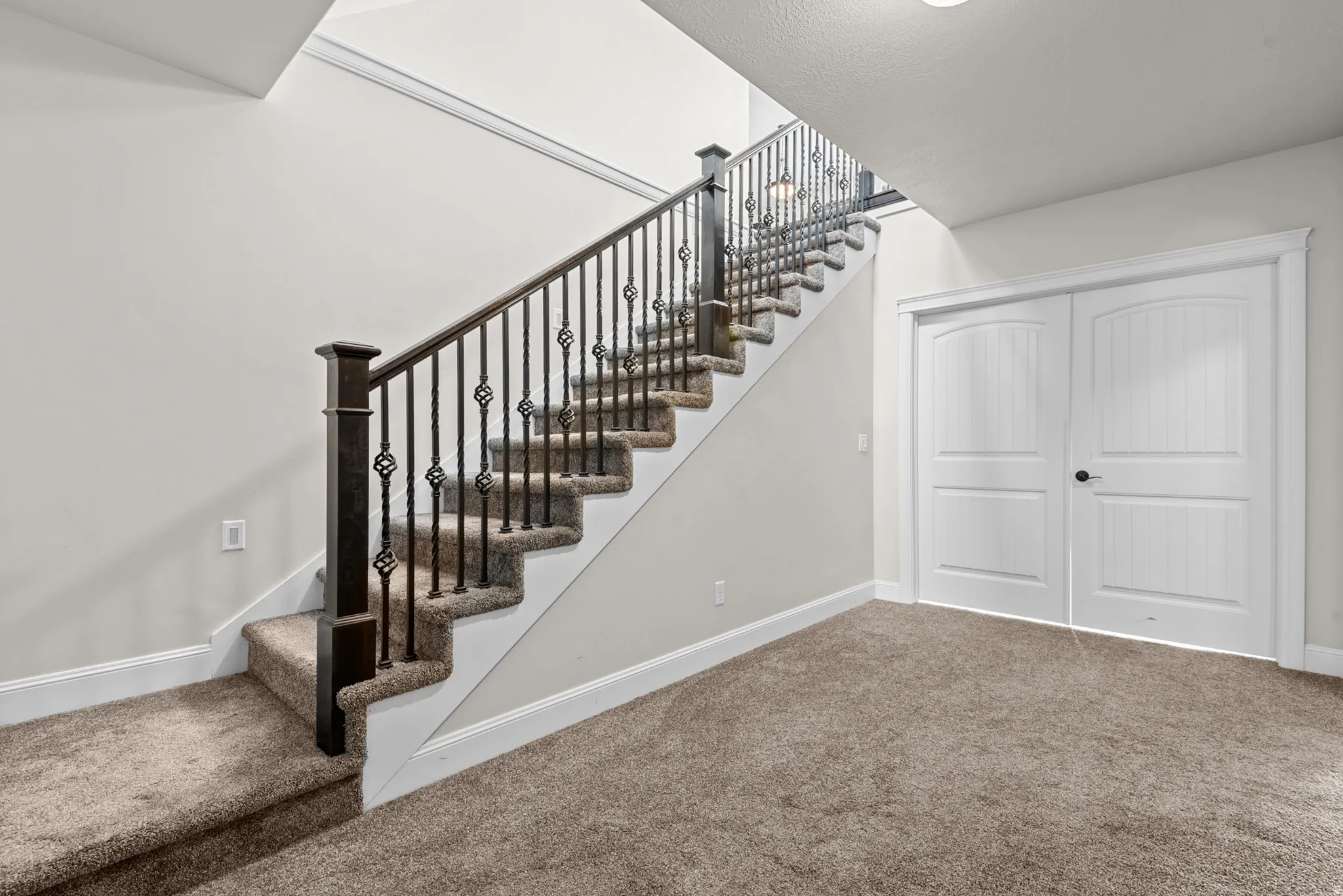 Carpeted staircase with decorative wrought iron balusters and dark wood newel posts