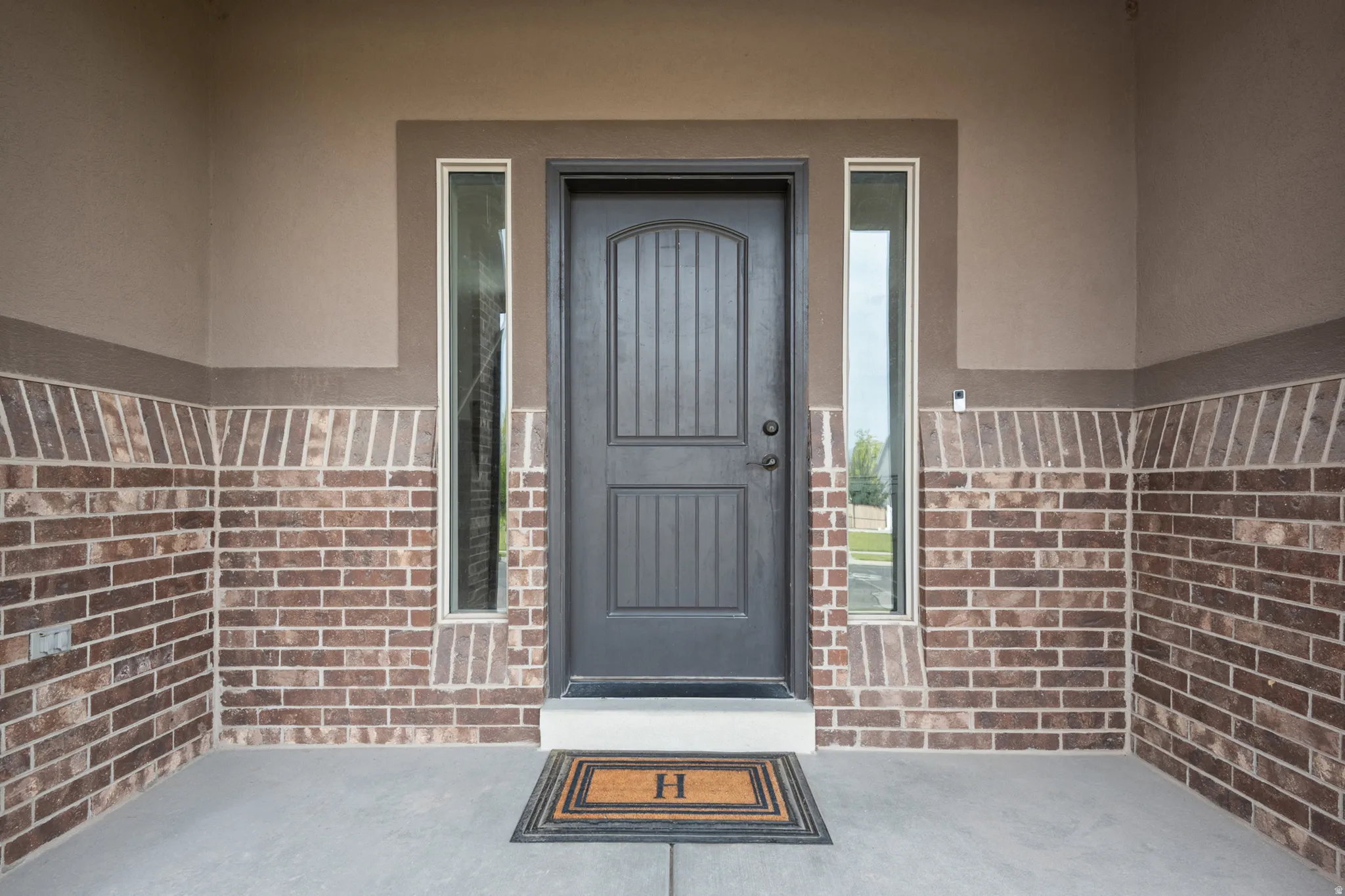 Arched panel entry door with vertical sidelight windows, brick lower wall, and stucco upper wall