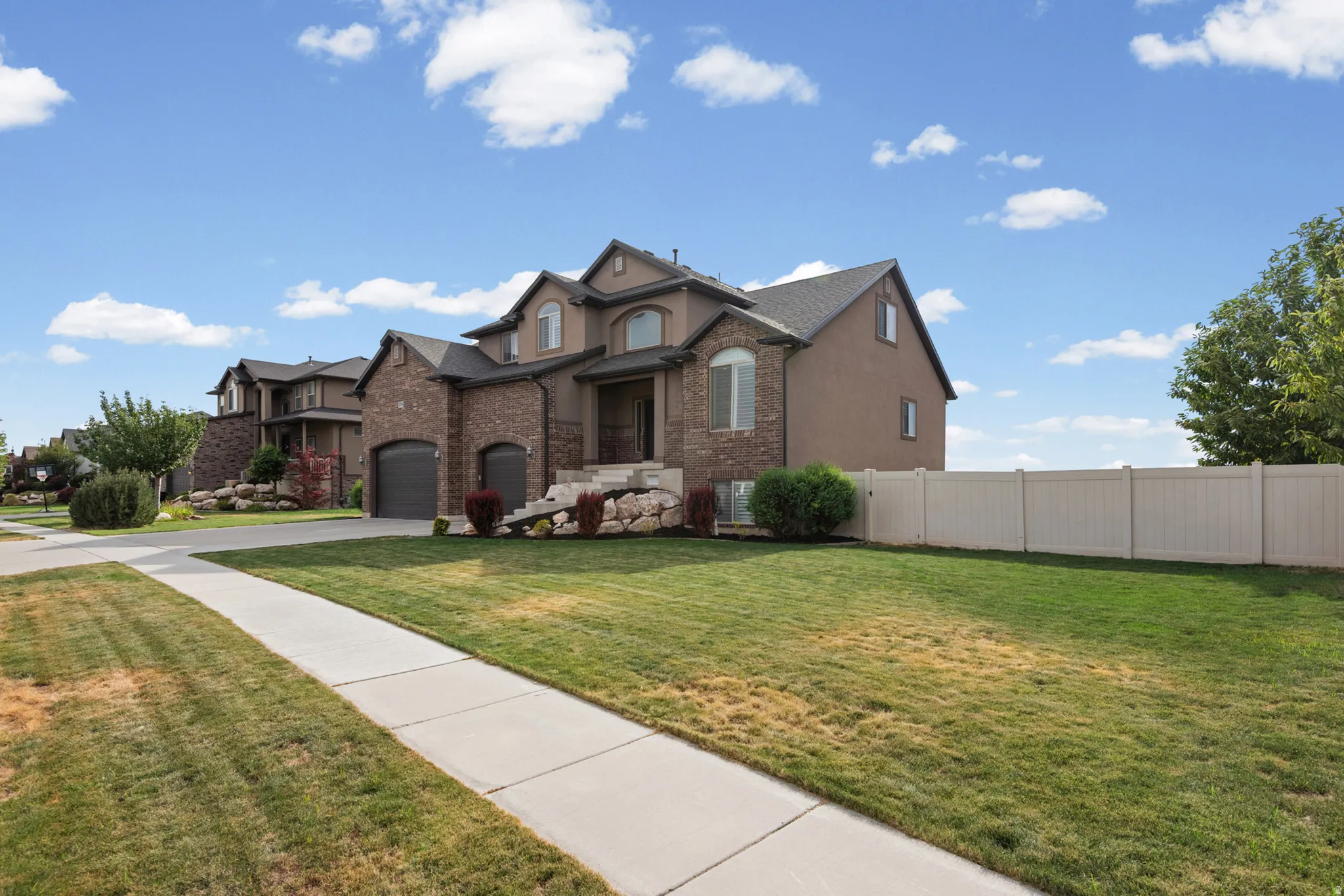 Brick Colonial home featuring a curved driveway, manicured lawn with mature landscaping, vinyl privacy fencing, and a multi-car garage with arched brick detailing