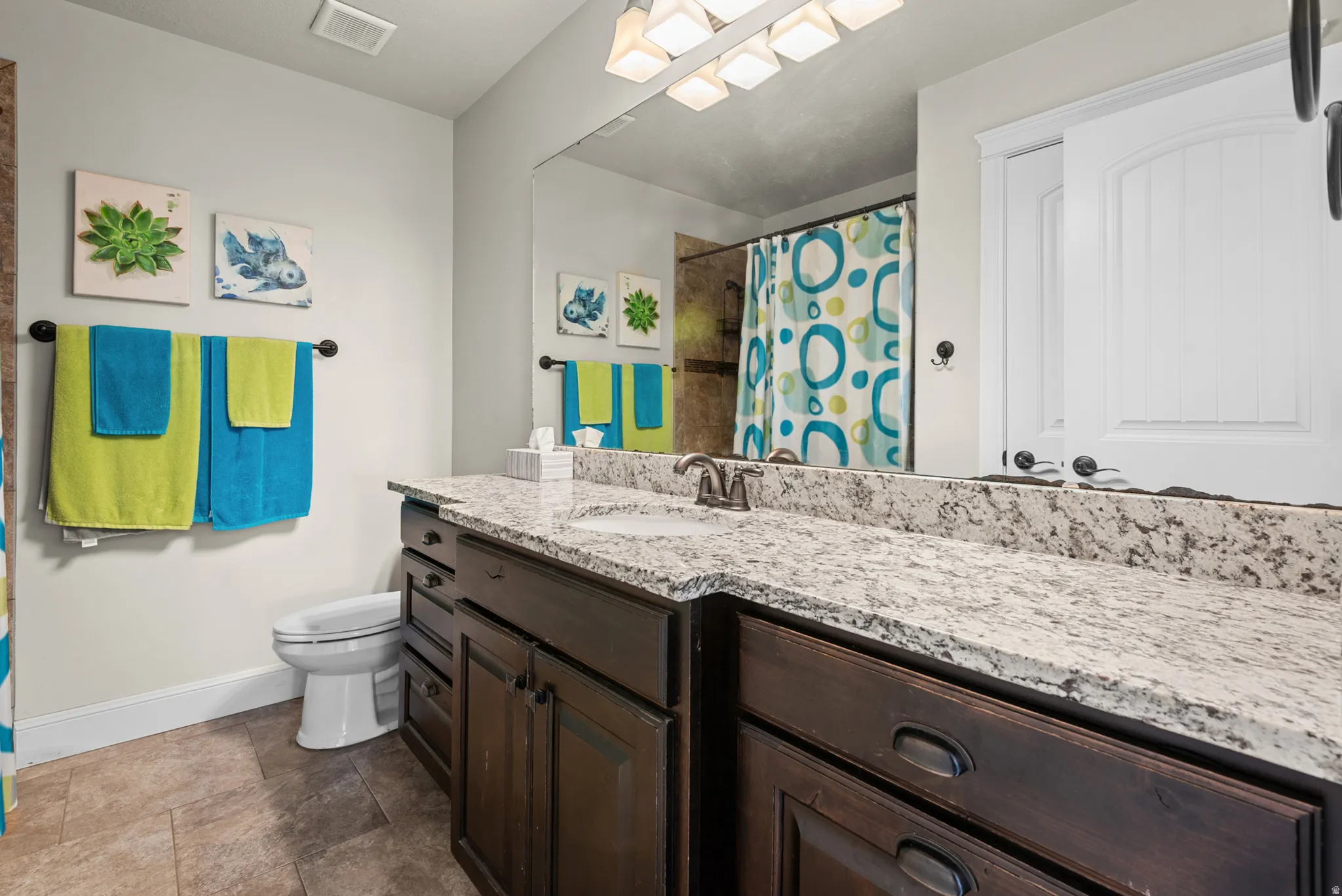 Bathroom featuring a single vanity with dark wood-finish cabinetry, a light-toned countertop, and a large wall-mounted mirror
