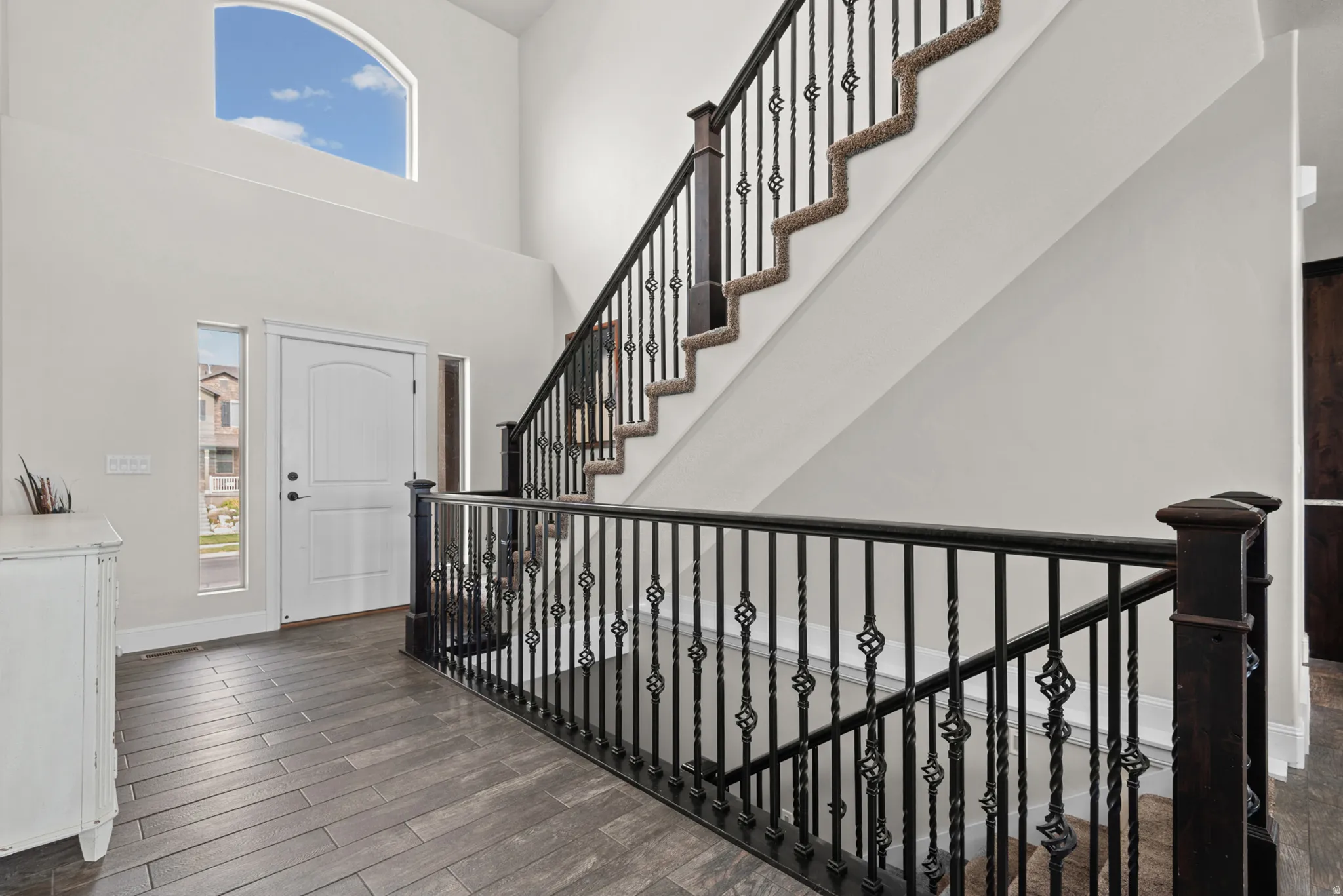 Entryway featuring a high ceiling, arched window, wood-finish flooring, and a staircase with an ornamental iron railing