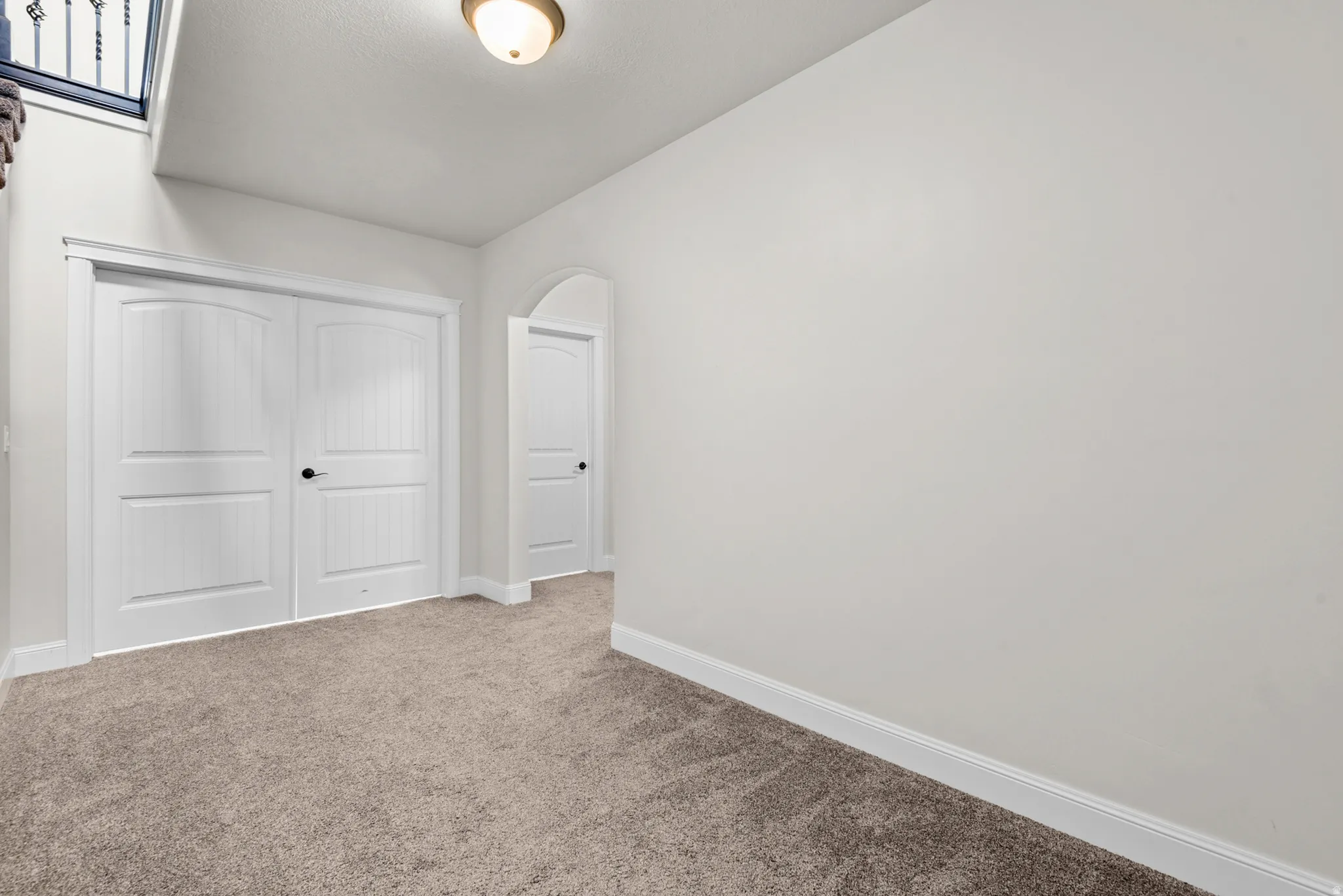Neutral tone carpeting, white interior doors, arched doorway, and overhead lighting fixture