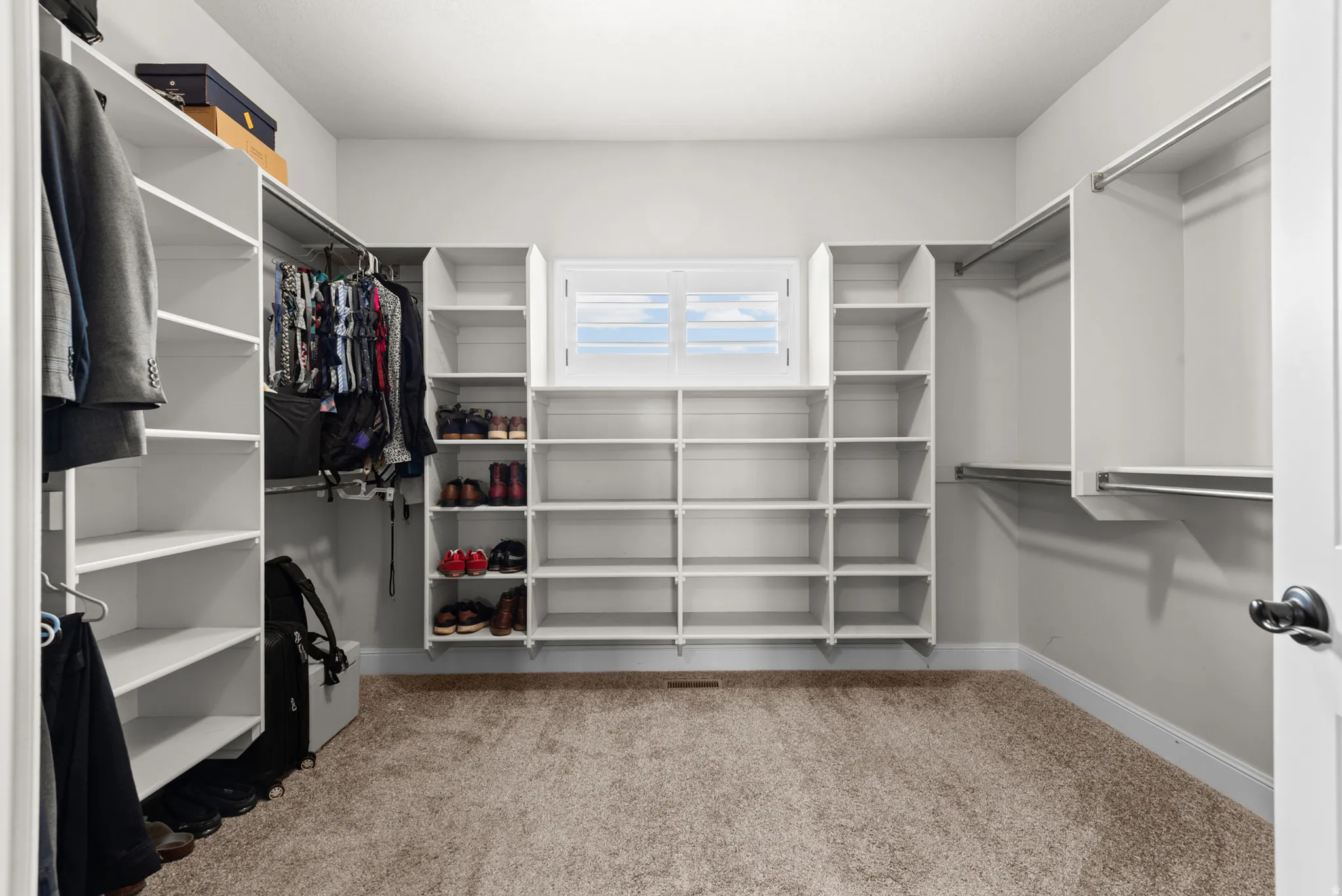 Built-in white shelving, integrated hanging rods, and a window with white shutters