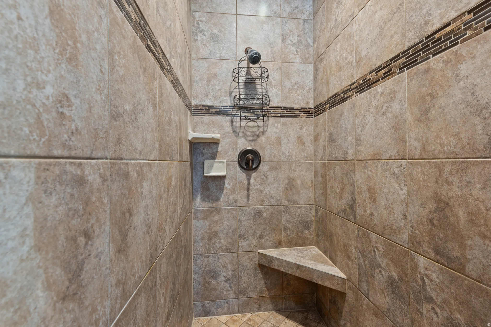 Tiled shower enclosure featuring a decorative mosaic accent band, built-in corner bench, and oil-rubbed bronze fixtures