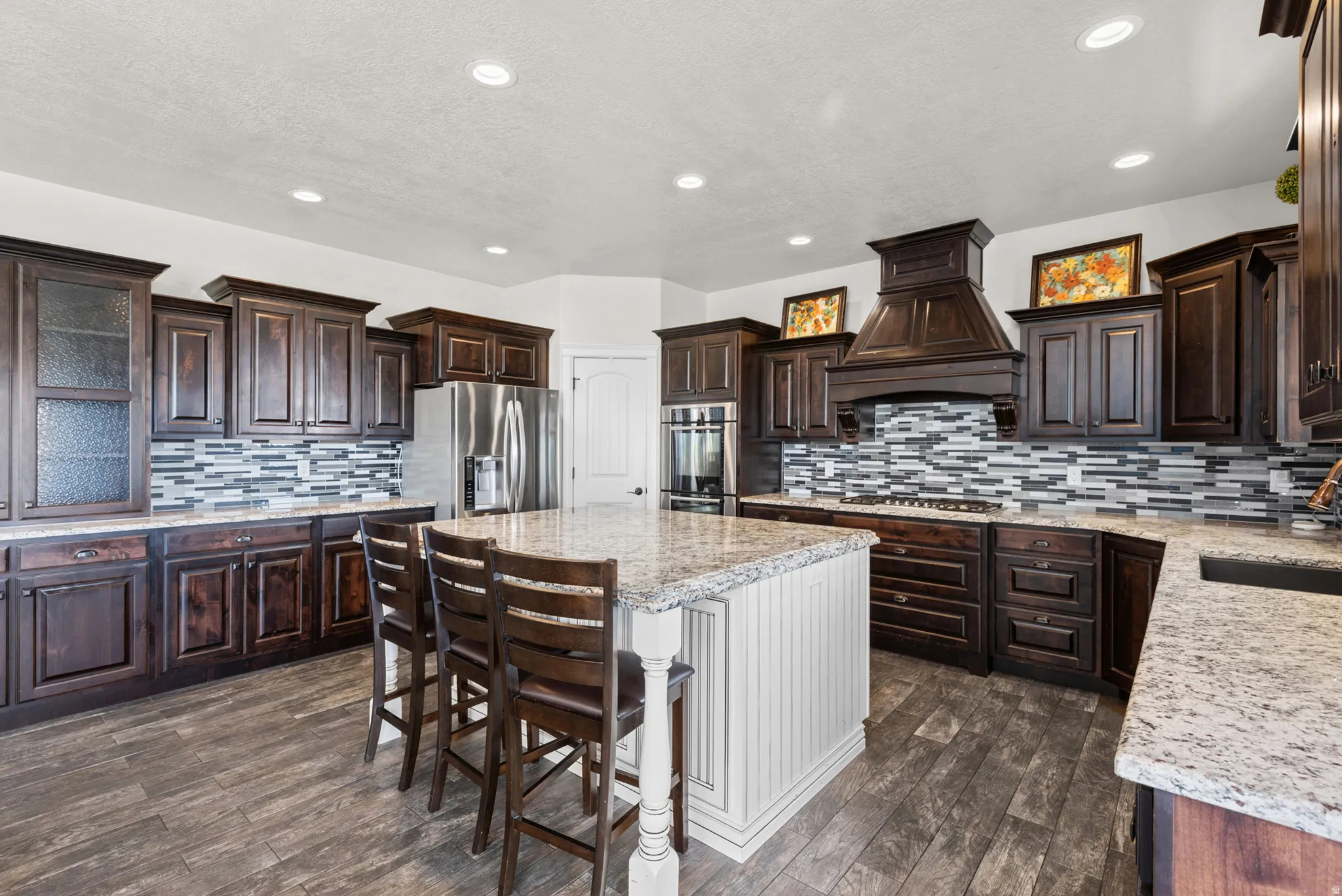 Gourmet kitchen featuring dark wood cabinetry with glass-front upper cabinets, stainless steel appliances, a decorative tile backsplash, and granite countertops