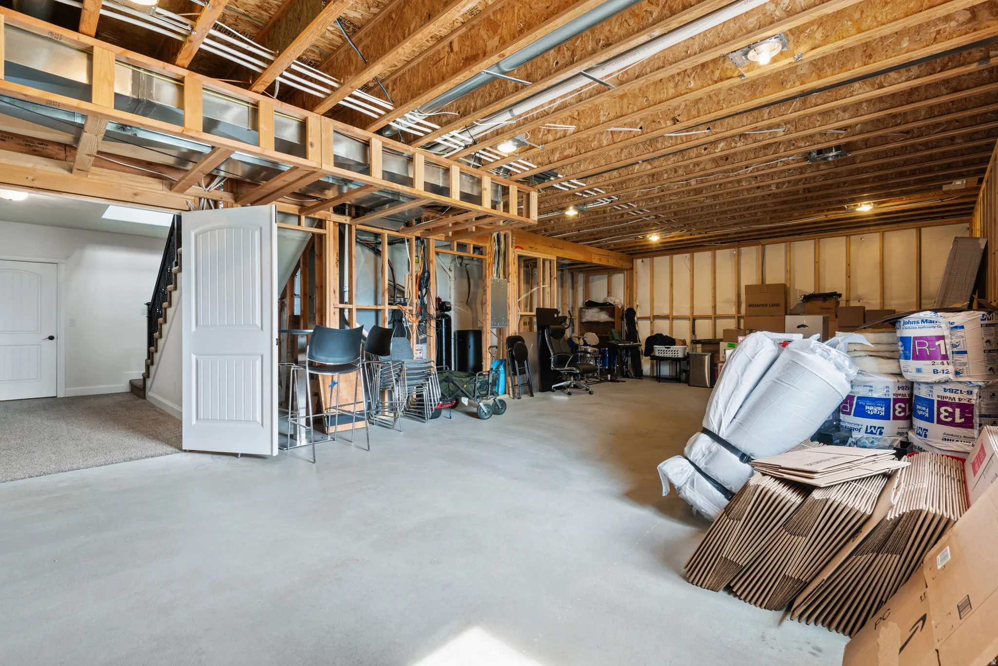Unfinished basement with exposed wood framing, concrete flooring, and an interior staircase with black railing