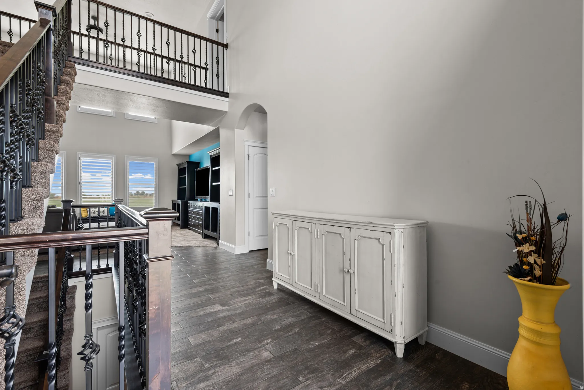 Two-story foyer featuring dark wood-finish flooring, an arched doorway, and an open upper-level walkway with dark metal balusters