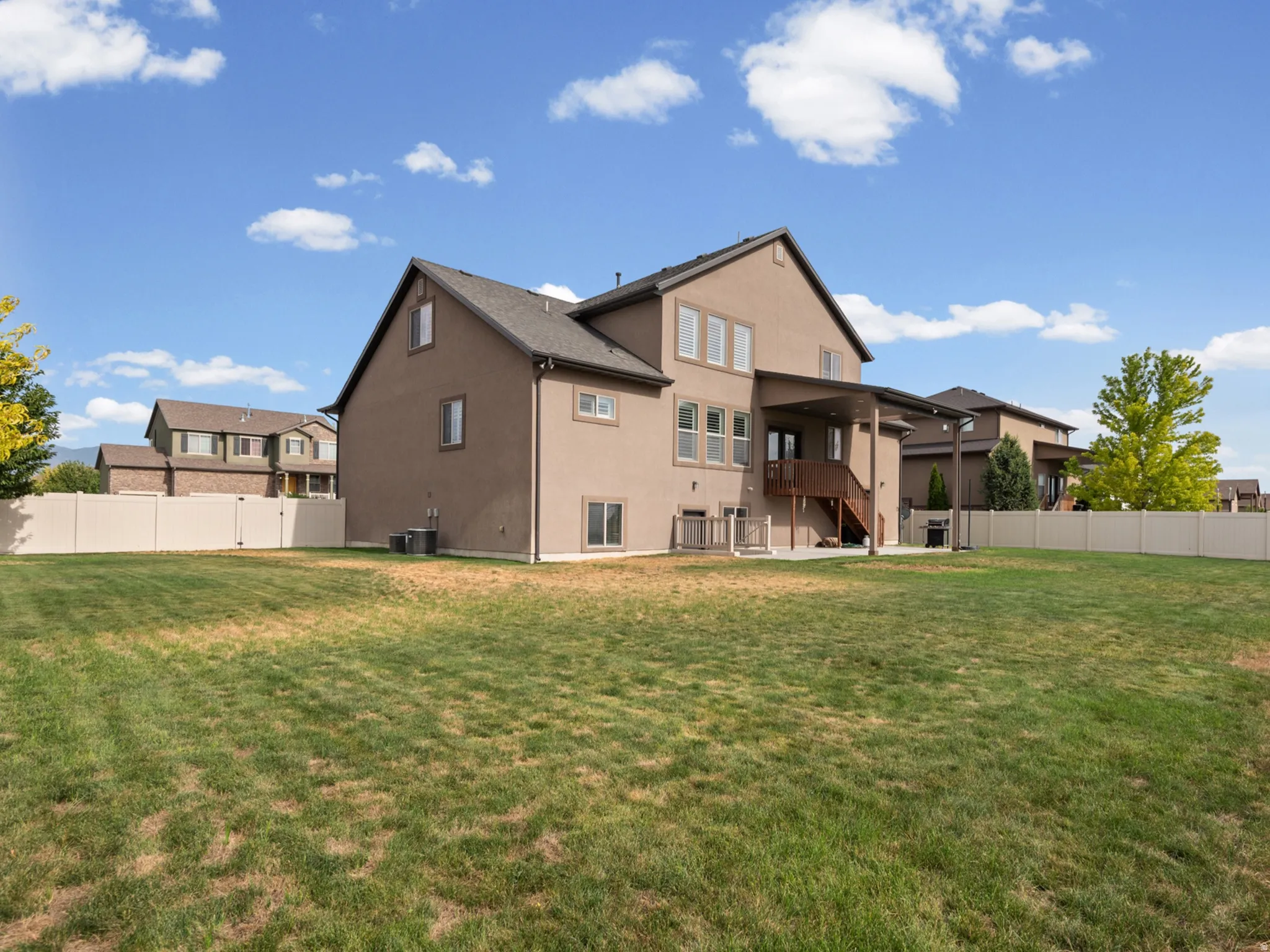 Expansive yard with privacy fencing, two-story stucco exterior, covered patio, and exterior stairs