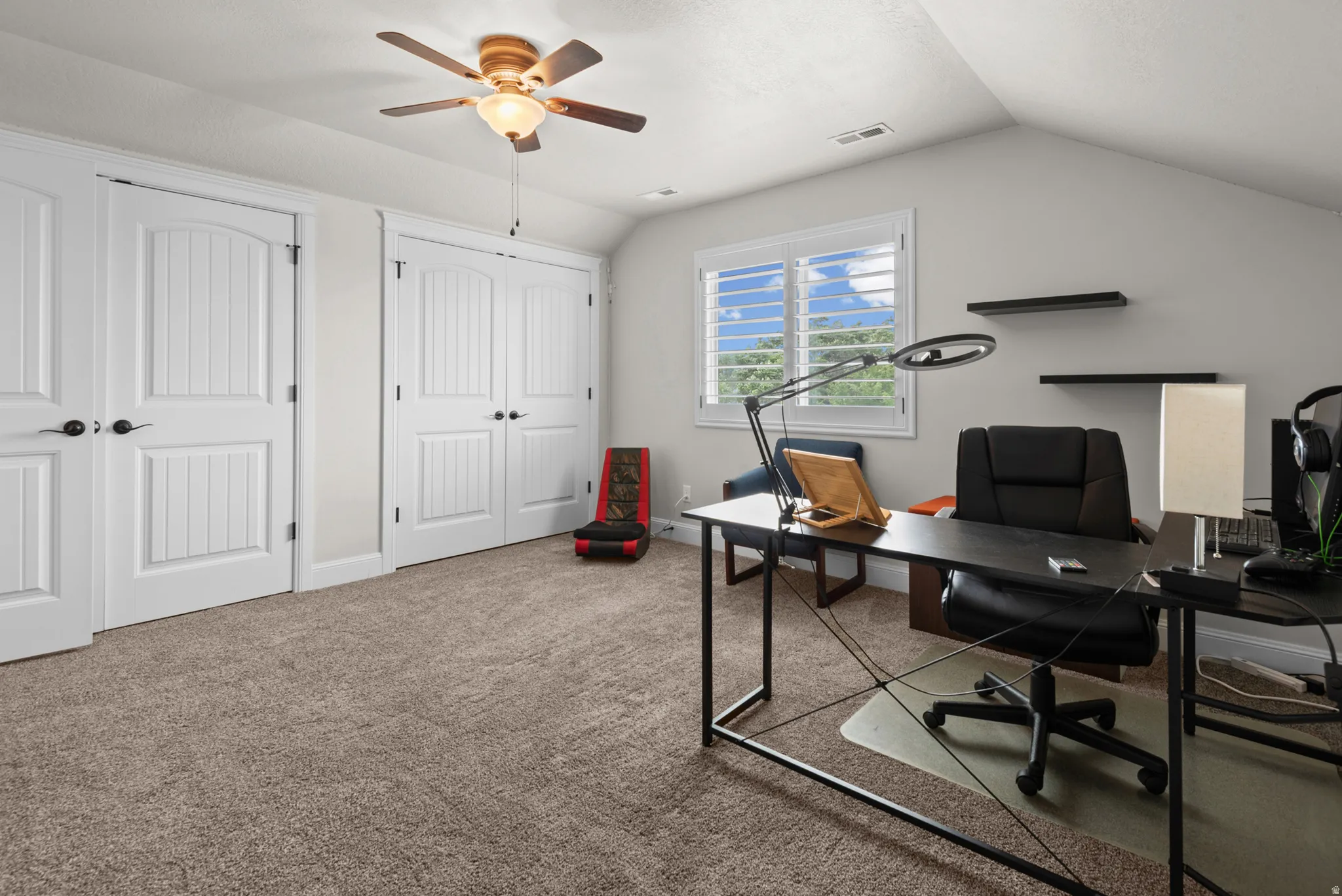 Vaulted ceiling, ceiling fan with integrated lighting, window with plantation shutters, two sets of bi-fold closet doors, and plush carpet flooring