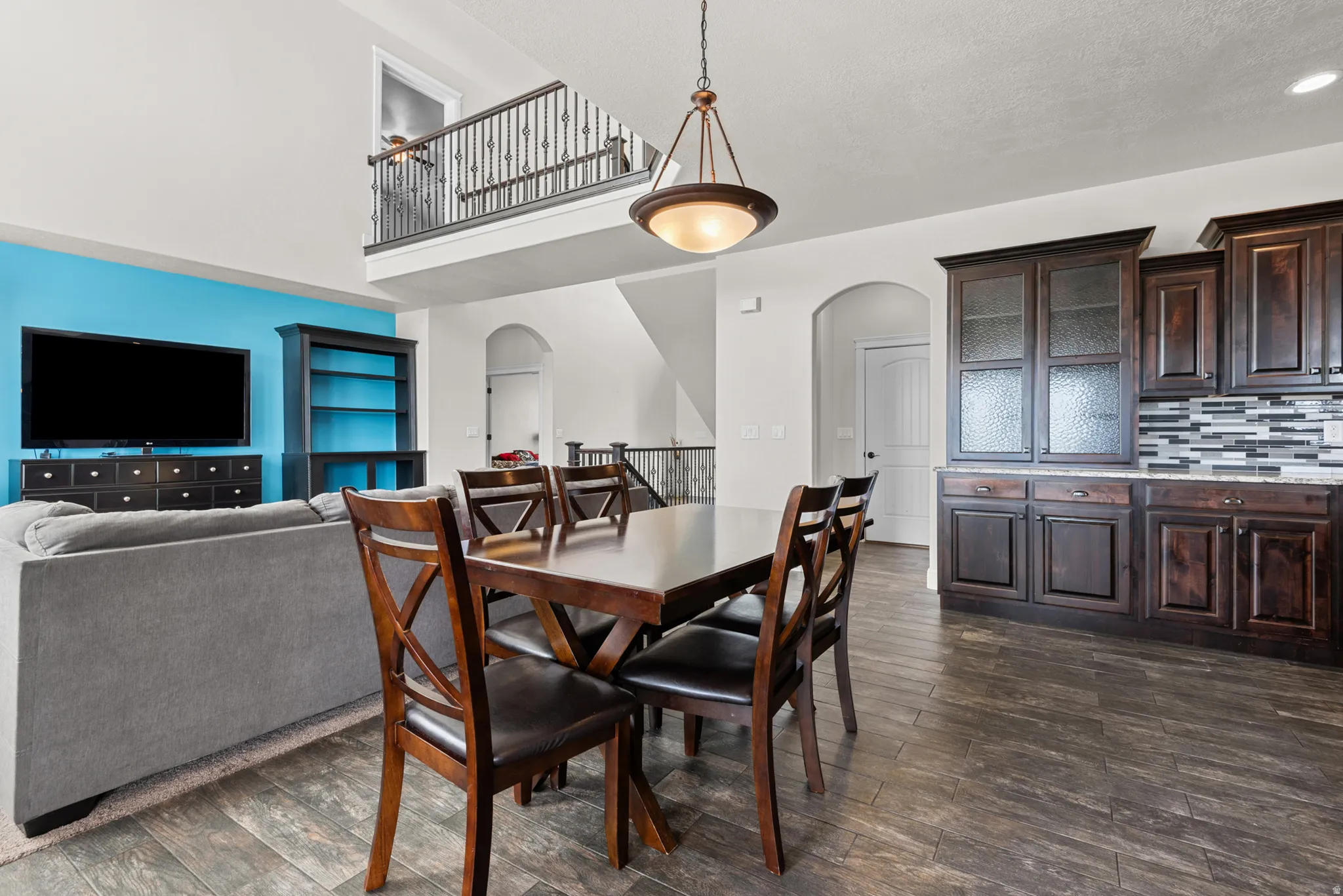 Open-concept living space featuring high ceilings, a second-story balcony with wrought iron railing, dark wood-finish flooring, and built-in cabinetry with a tiled backsplash