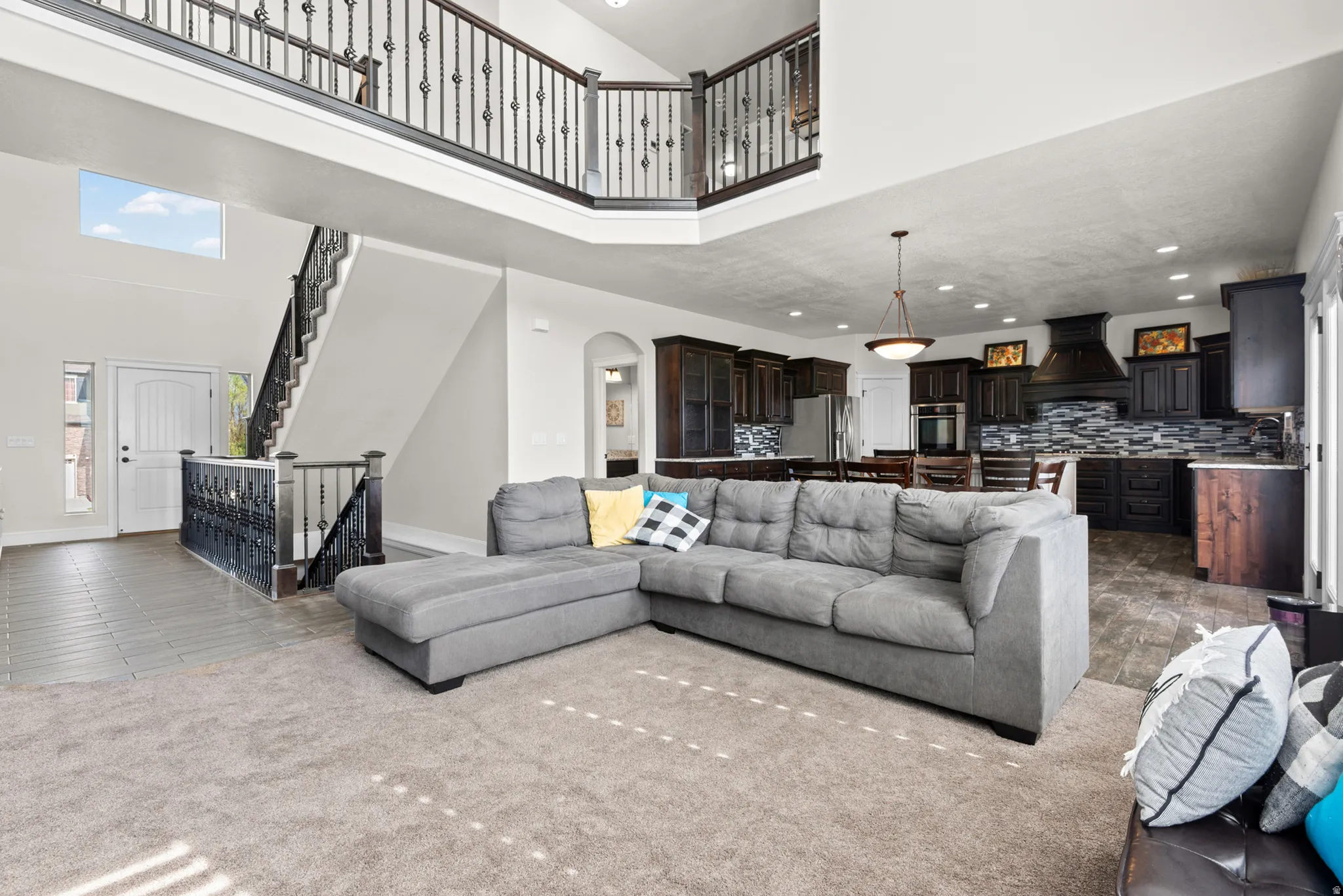 Open-concept living area featuring a two-story atrium with skylights, neutral tile flooring throughout, and a gray upholstered sectional sofa