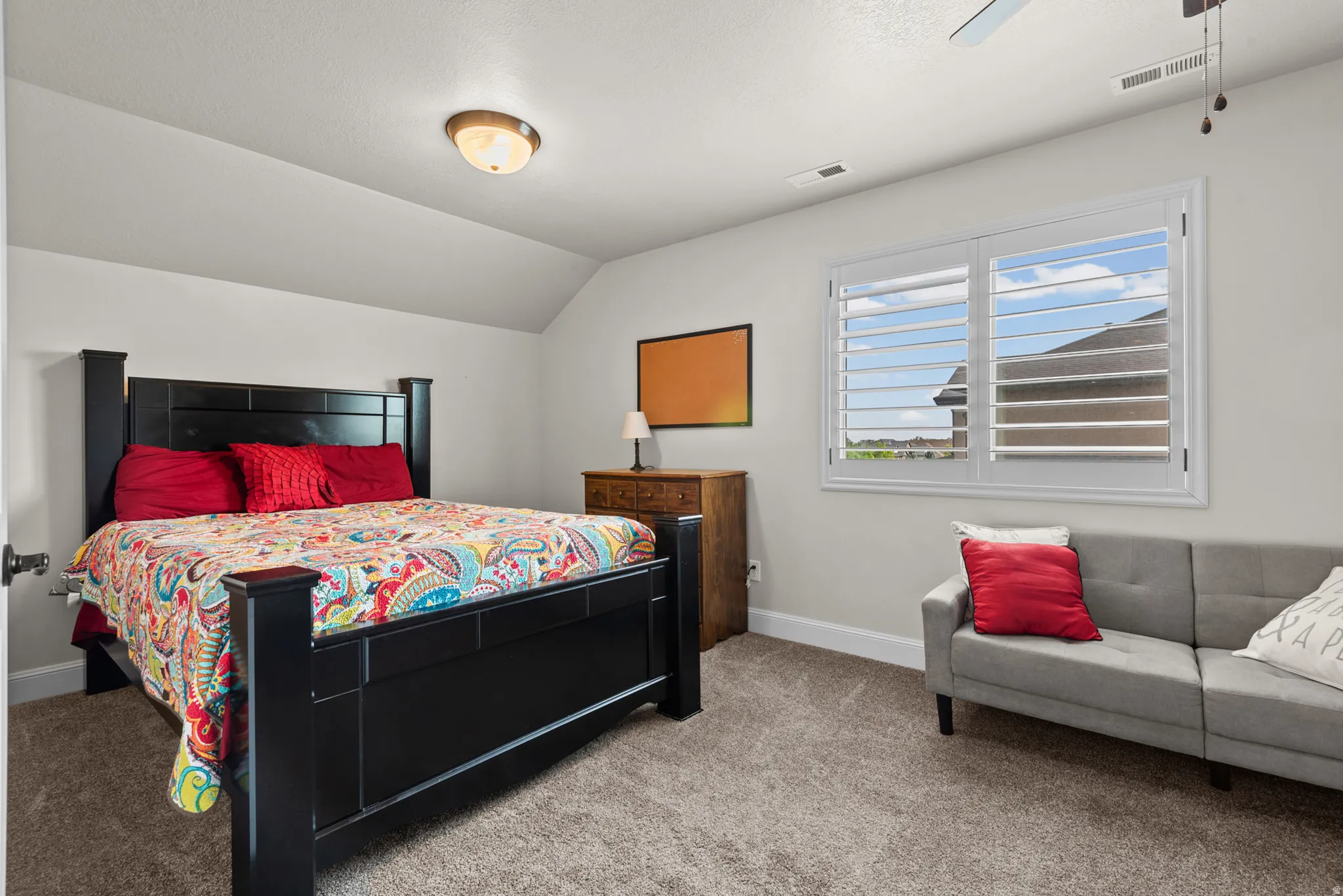 Carpeted room with a vaulted ceiling, white walls, and a window featuring plantation shutters