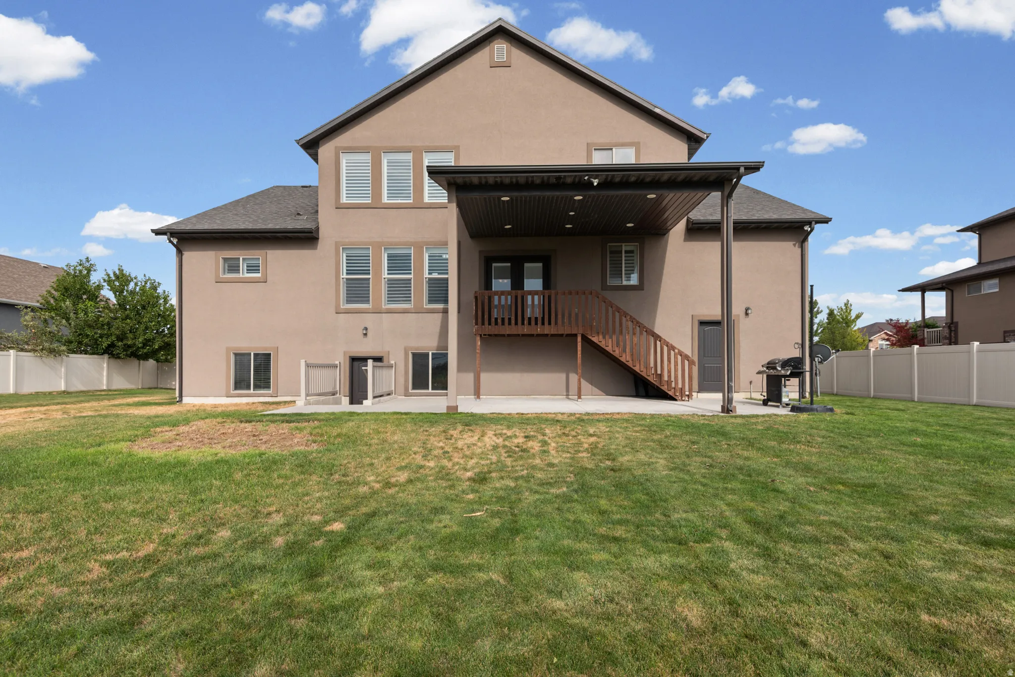 Expansive backyard featuring a covered patio, upper-level deck with wood railing, and a full-height privacy fence