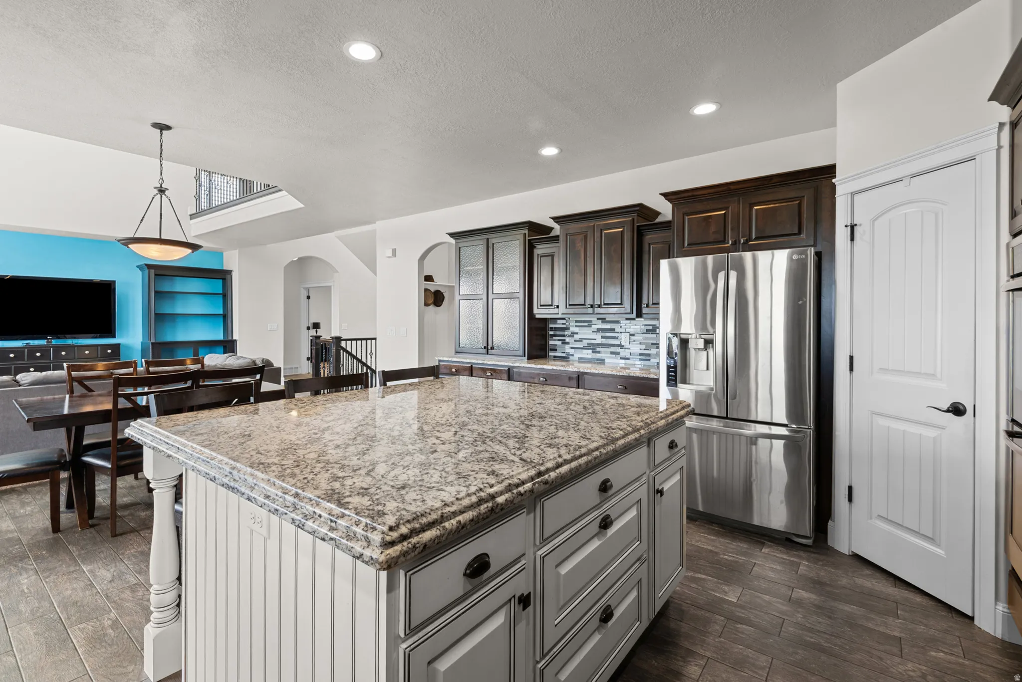 Kitchen island with a light-toned countertop, wood-finish flooring, dark wood cabinetry, a mosaic tile backsplash, and stainless steel appliances