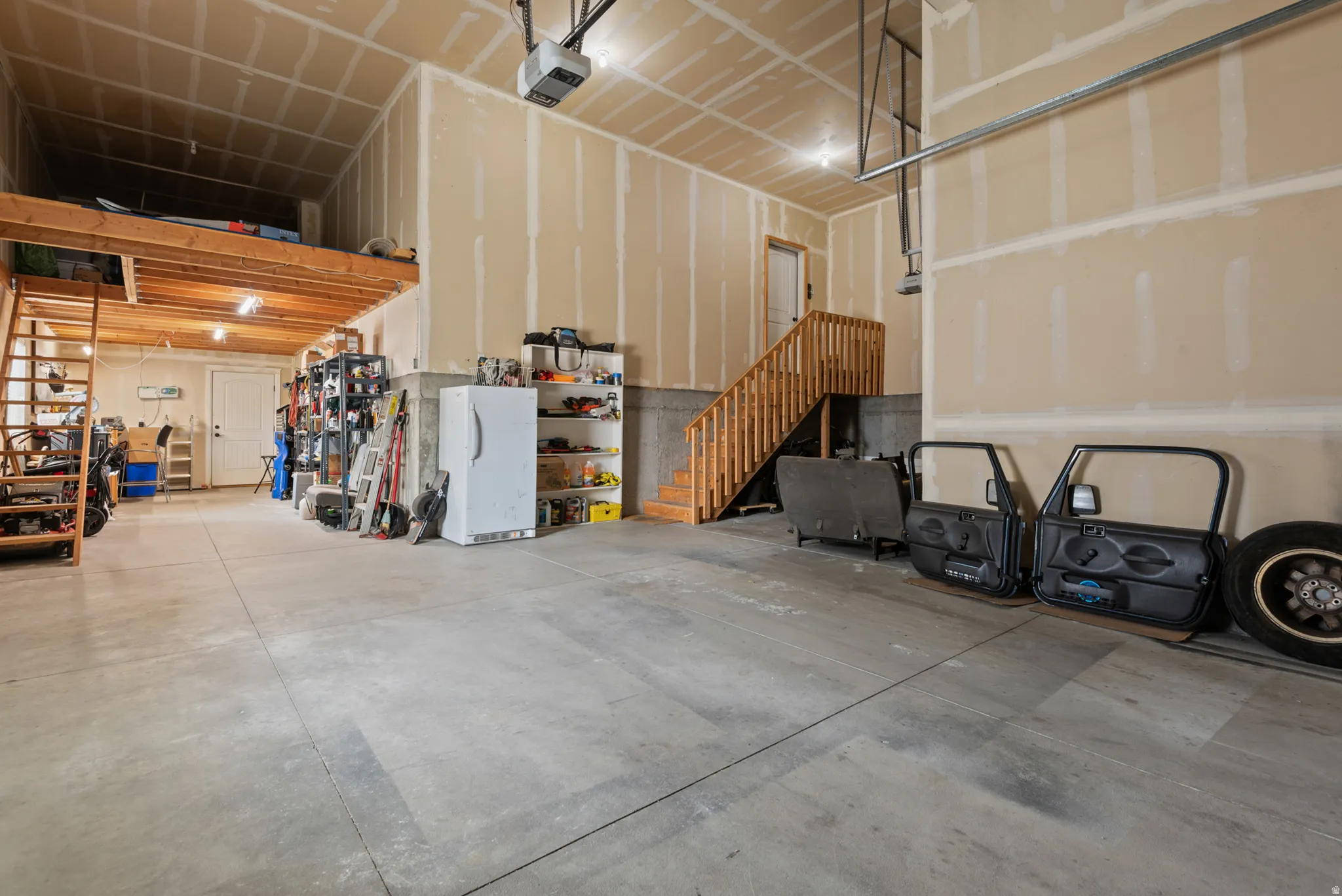 Garage with concrete flooring, natural wood staircase, wood-finish overhead storage, high ceilings, and recessed lighting