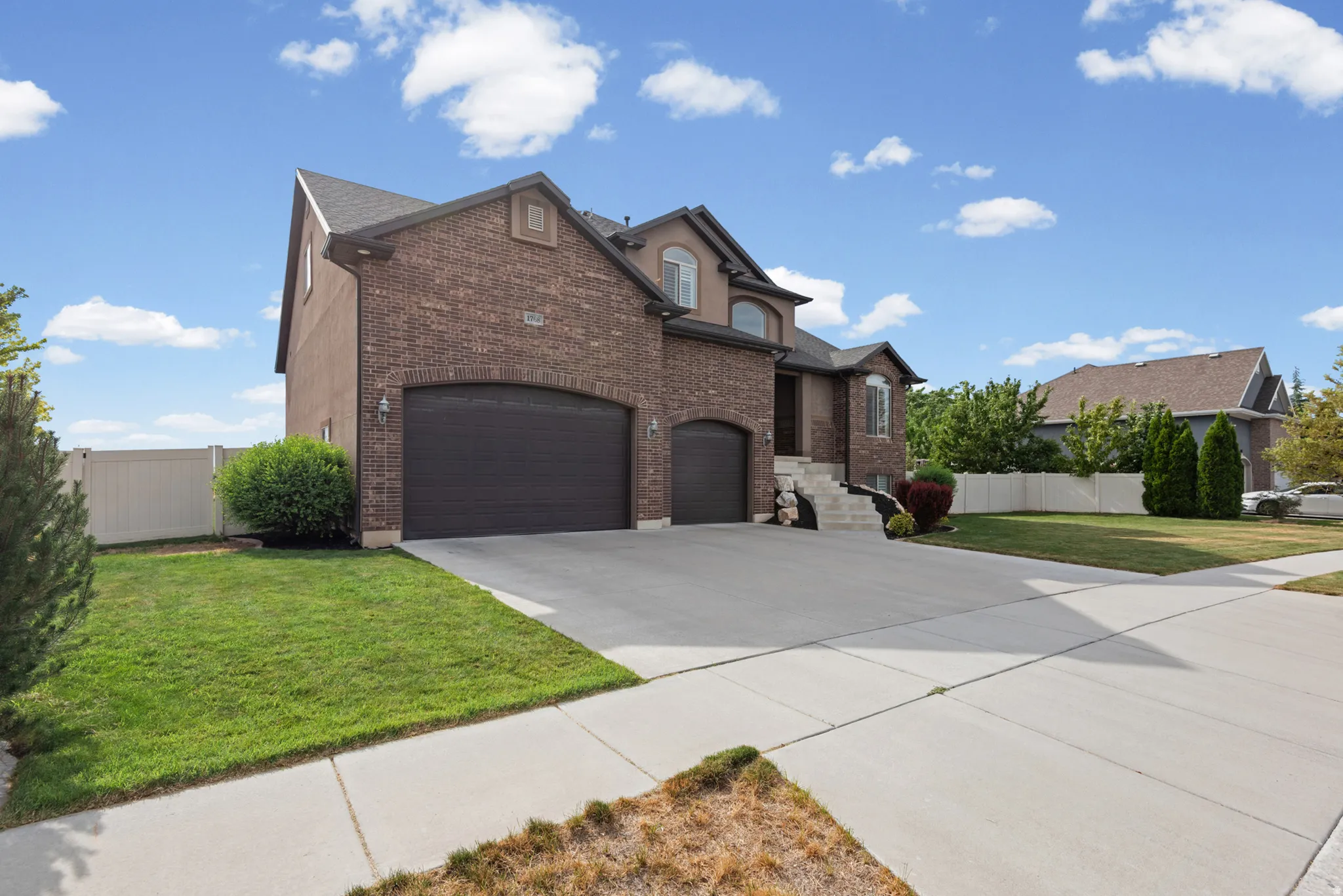Brick and stucco exterior with multiple gables, arched garage doors, a concrete driveway, and a front lawn with mature landscaping