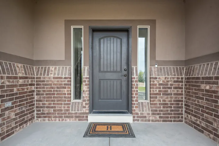Arched panel entry door with vertical sidelight windows, brick lower wall, and stucco upper wall