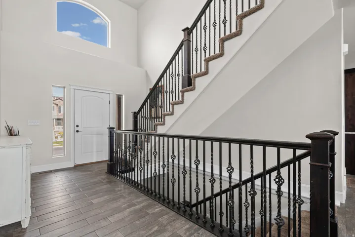 Entryway featuring a high ceiling, arched window, wood-finish flooring, and a staircase with an ornamental iron railing