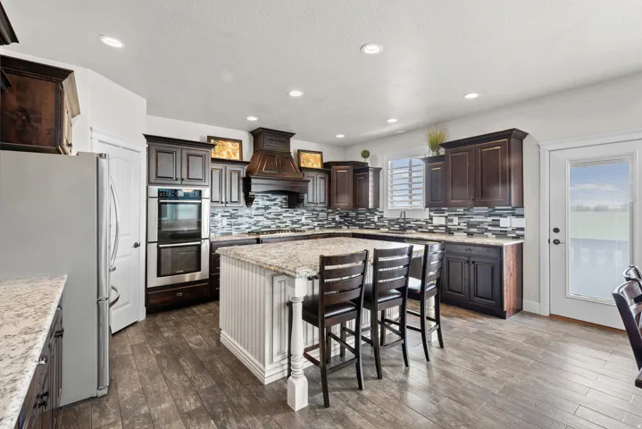 Chef's kitchen featuring custom dark cabinetry with glass-front upper displays, stainless steel double wall ovens, a professional-style range hood, quartz countertops, and a large center island with seating