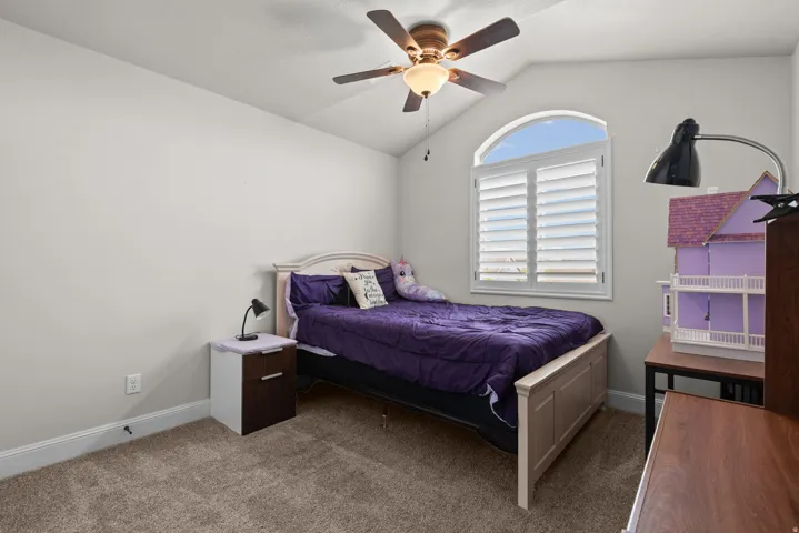 Arched window with plantation shutters, vaulted ceiling, and ceiling fan with integrated lighting