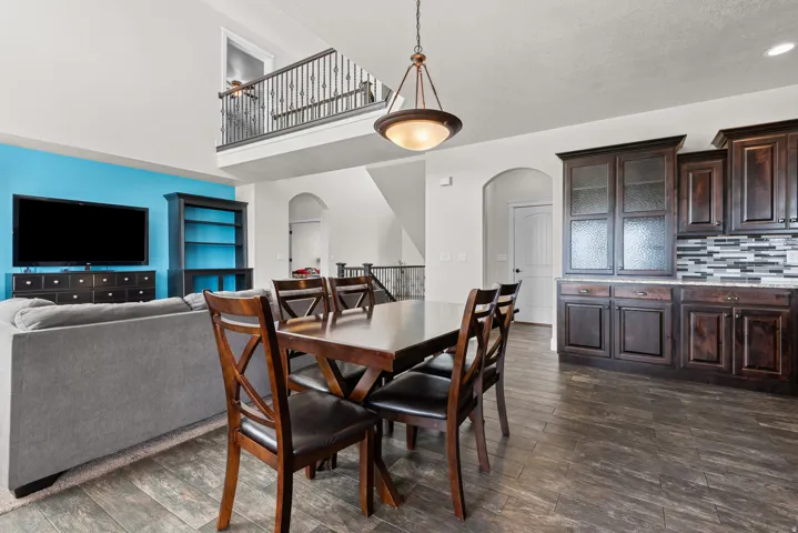 Open-concept living space featuring high ceilings, a second-story balcony with wrought iron railing, dark wood-finish flooring, and built-in cabinetry with a tiled backsplash