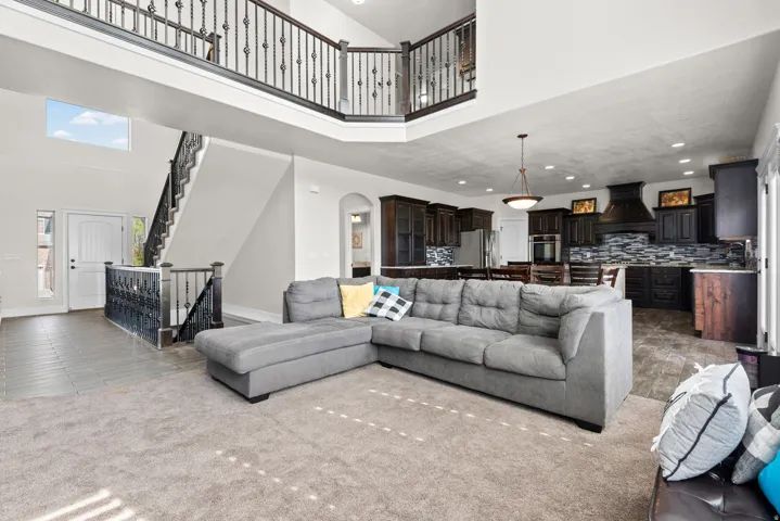 Open-concept living area featuring a two-story atrium with skylights, neutral tile flooring throughout, and a gray upholstered sectional sofa